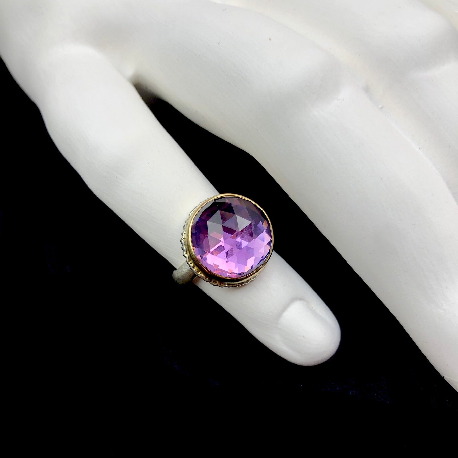 Round amethyst ring with ruffled stone setting shown on white ceramic finger