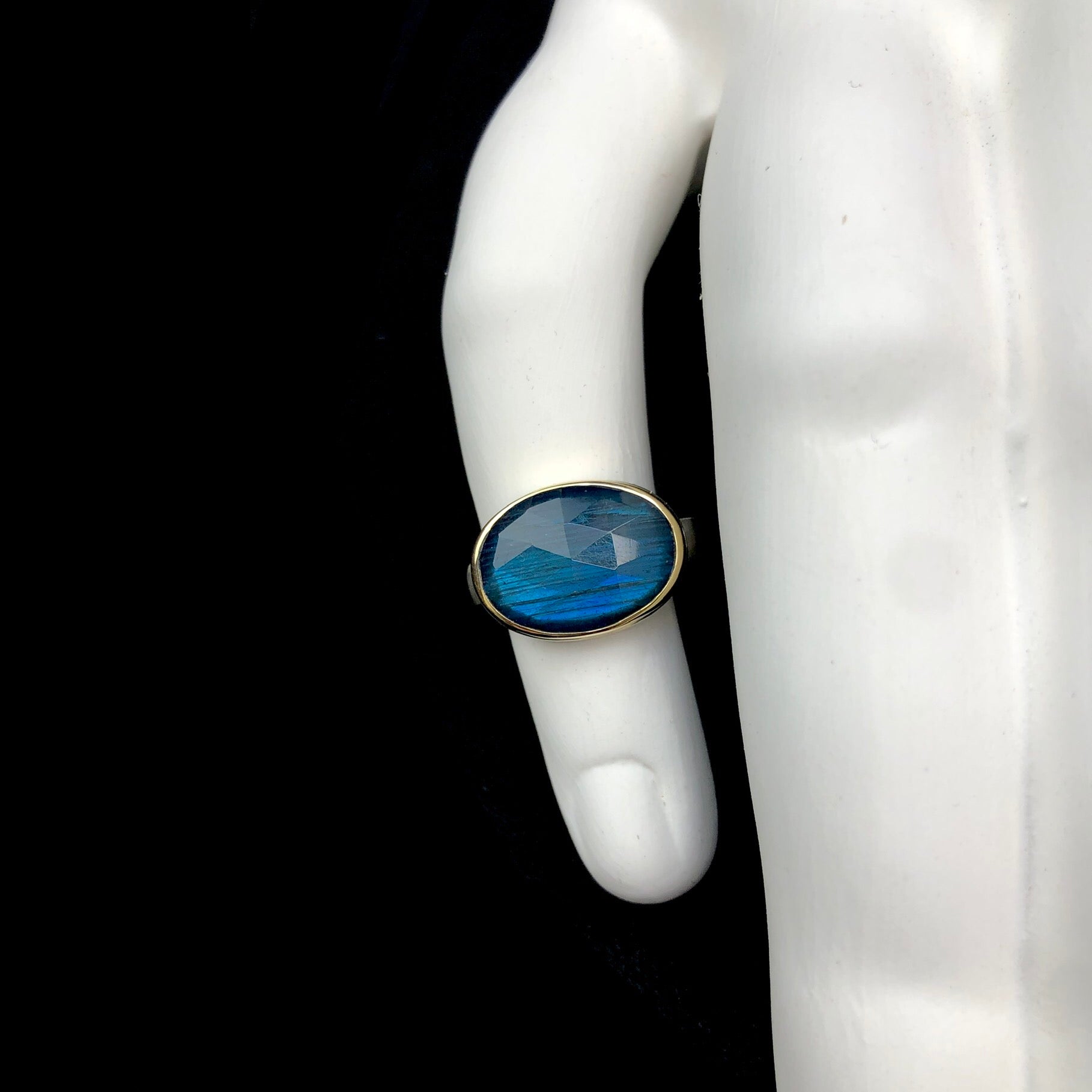 Front view of iridescent blueish green labradorite stone ring shown on white ceramic finger