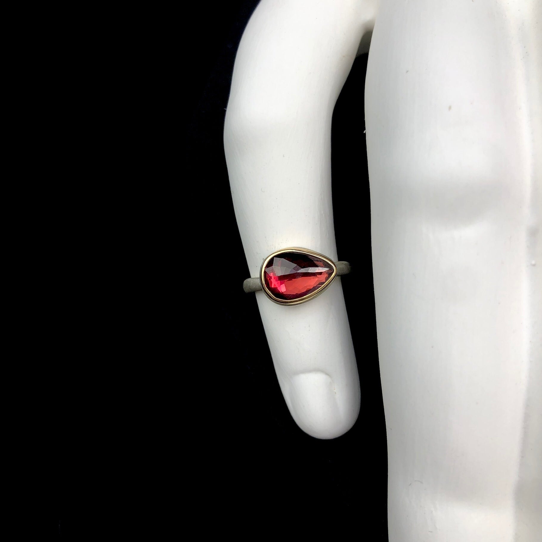 Red colored garnet stone ring with small facets on the surface shown on white ceramic hand