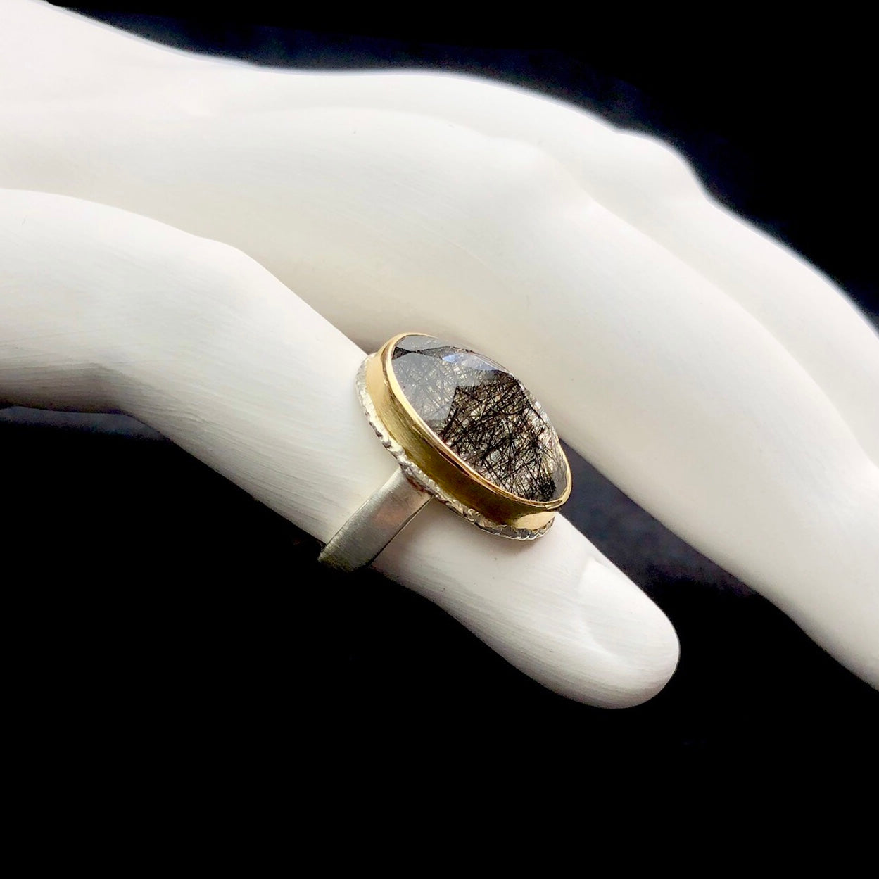 Side profile view of tourmalineted quartz ring on white ceramic finger