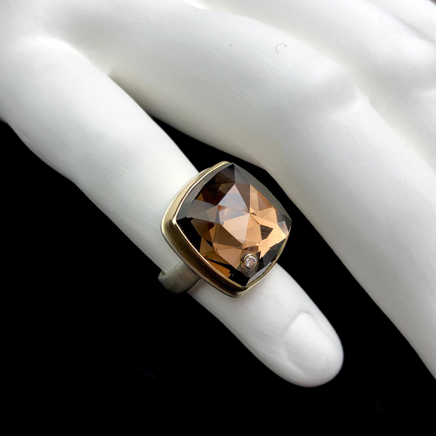 Front side view of diamond accent and signature band of smokey quartz ring shown on white sculpted ceramic finger