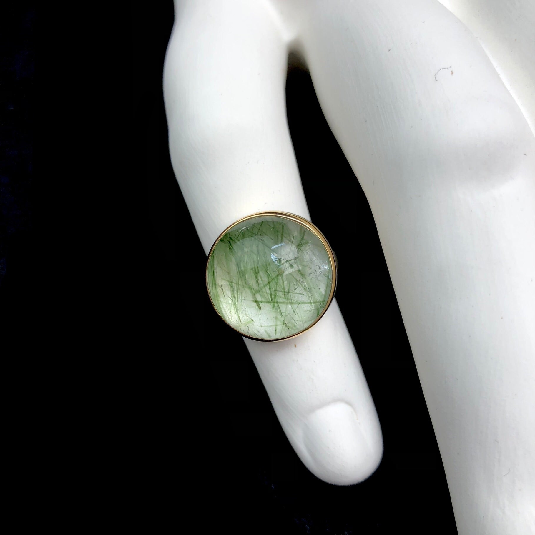 Round, light green prehnite stone shown on white ceramic finger