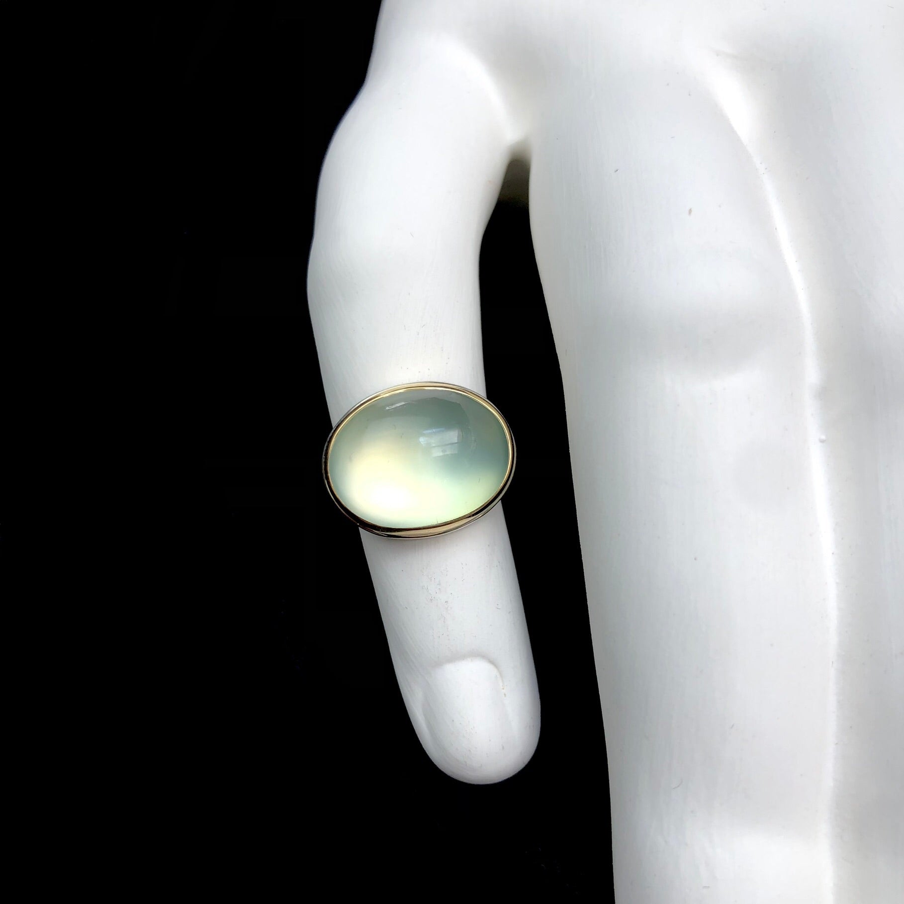 Top view of oval shaped, light green prehnite stone ring shown on white ceramic finger