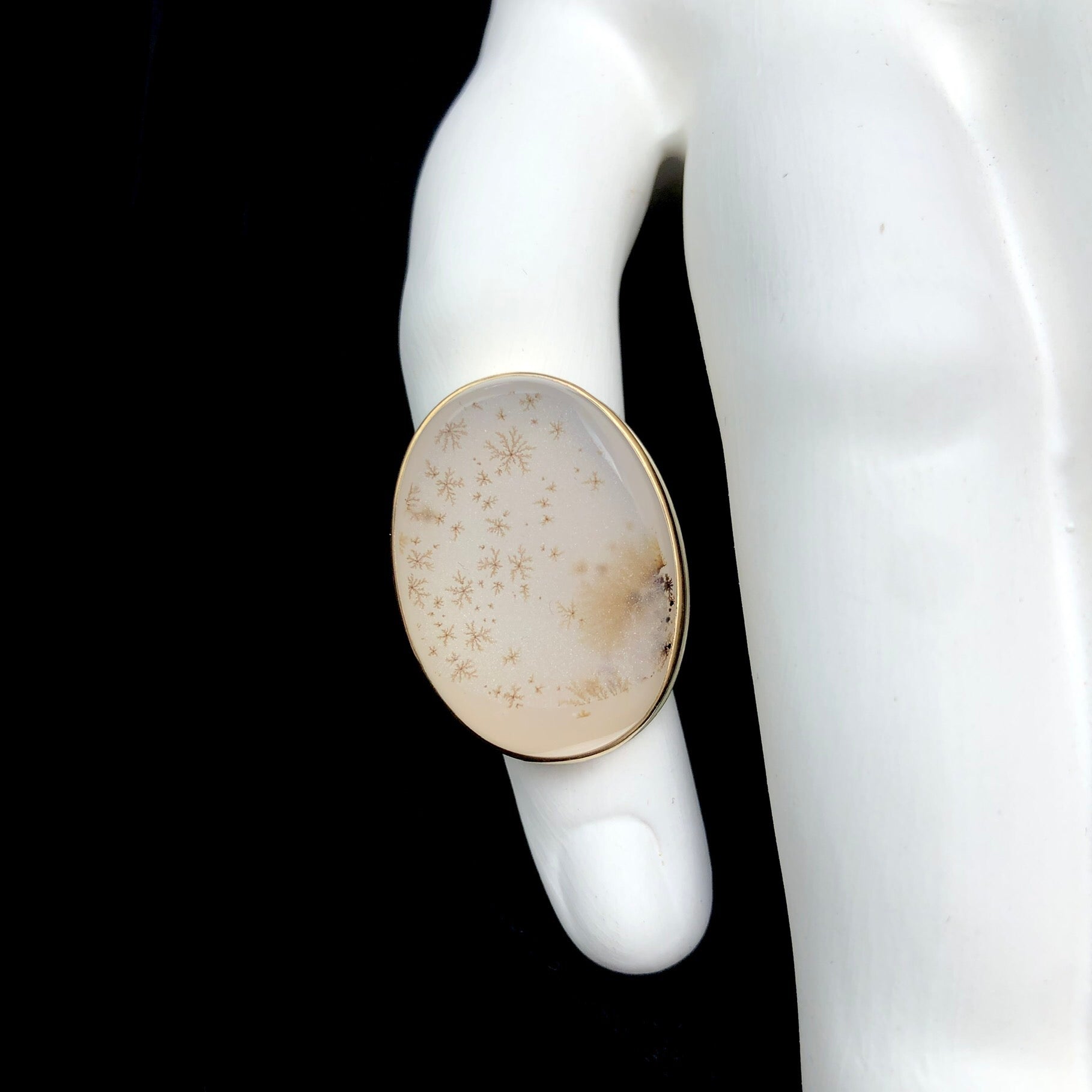 Brown dendritic accents on white crystalline druzy surface agate ring shown on white ceramic finger