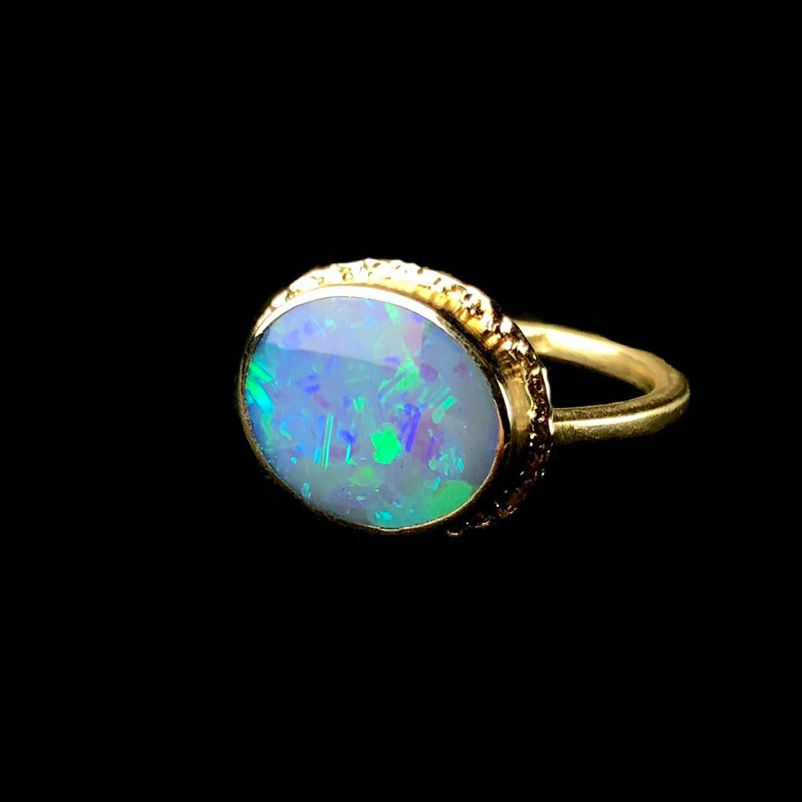 Oval shaped opal with iridescent flashes of green and blue color set in solid gold ring
