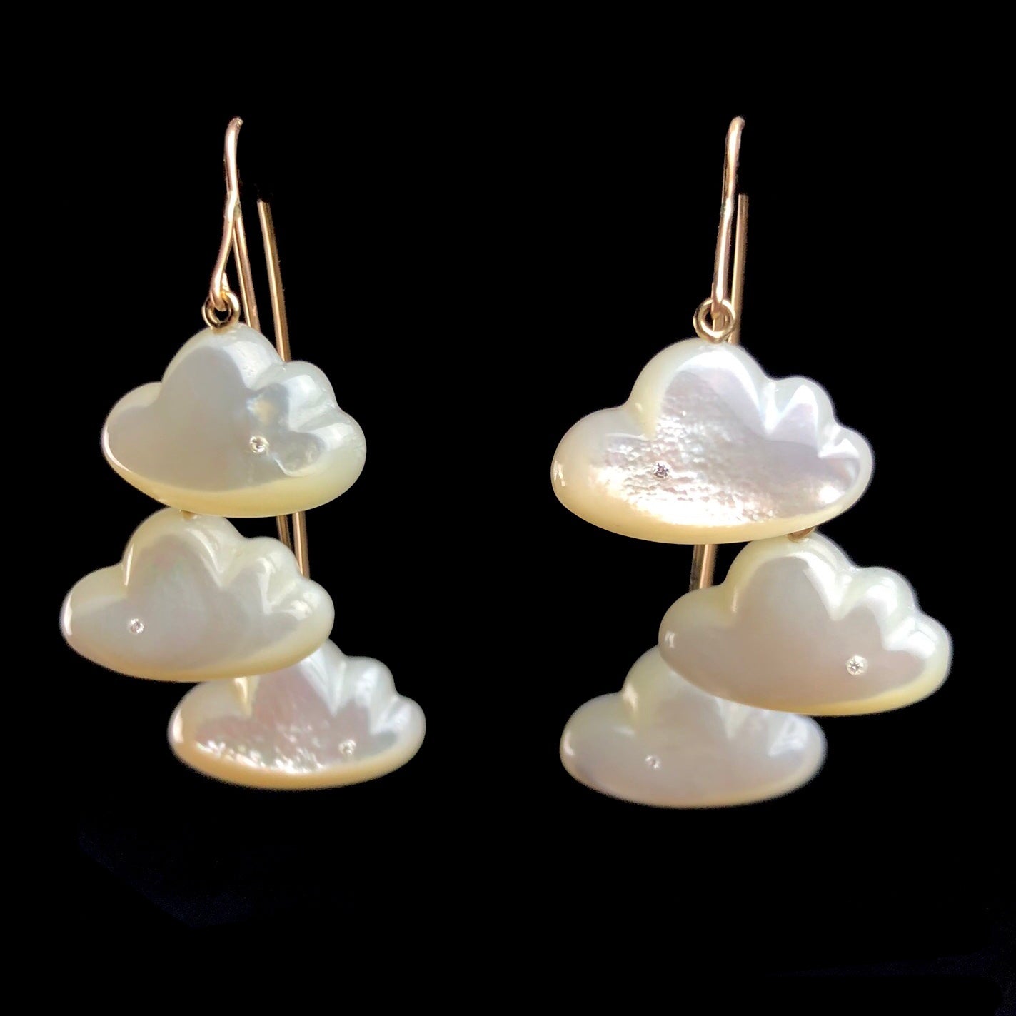 A pair of golden earrings each with three, white clouds hanging like chandeliers