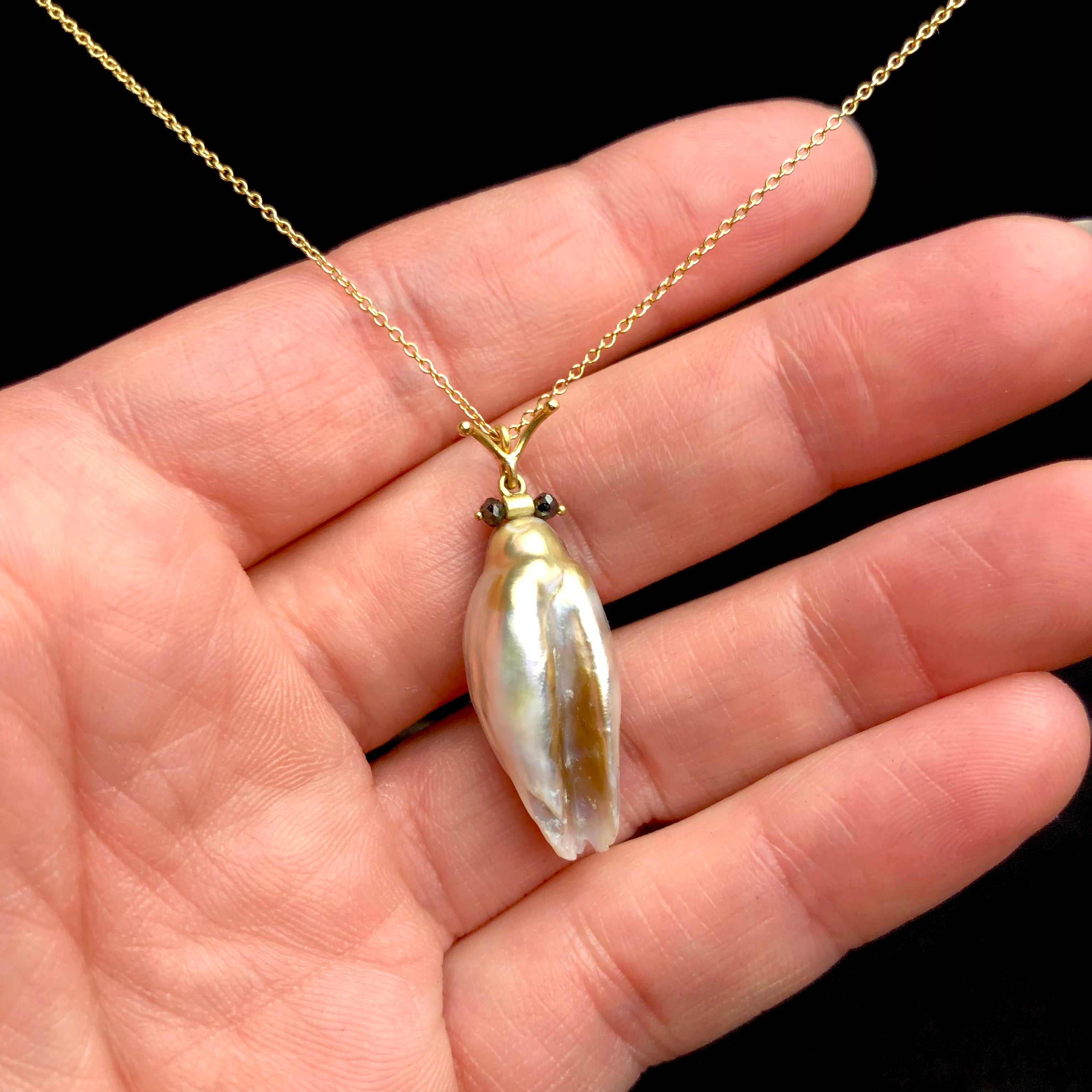 Golden pink pearl pendant with black diamond eyes and gold accents on chain shown in hand
