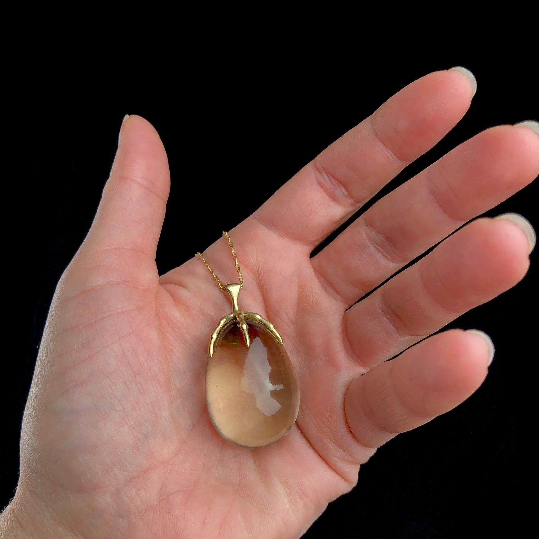 Egg shaped smokey grey colored quartz crystal held by a gold talon held in hand