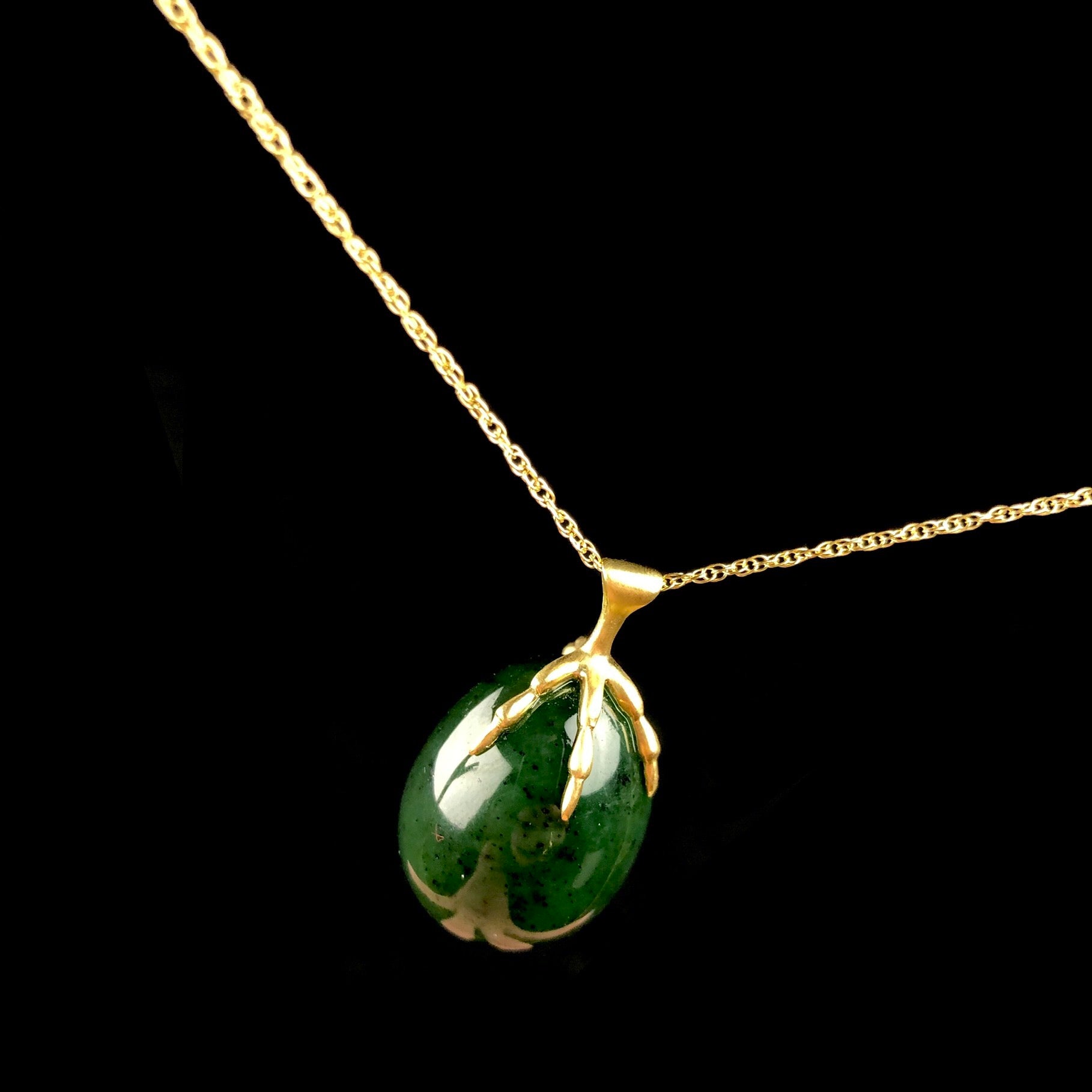 Green egg shaped stone held by a gold bird claw on gold chain