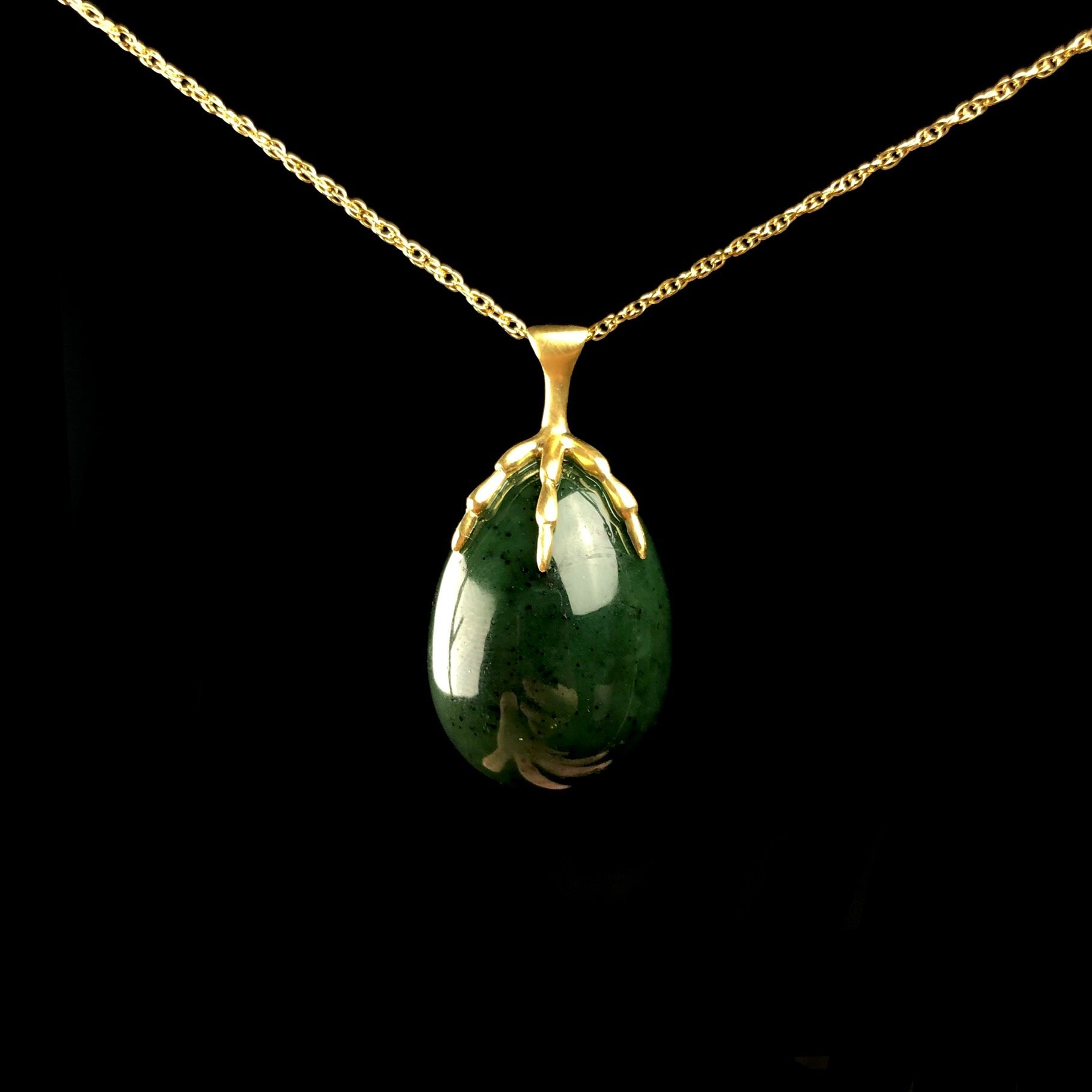 Green egg shaped stone held by a gold bird claw on gold chain