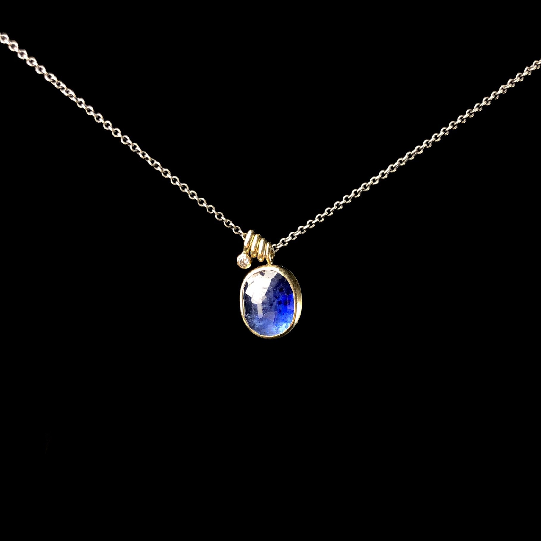 Blue oval stone with gold setting on blackened silver chain with gold accents and diamond