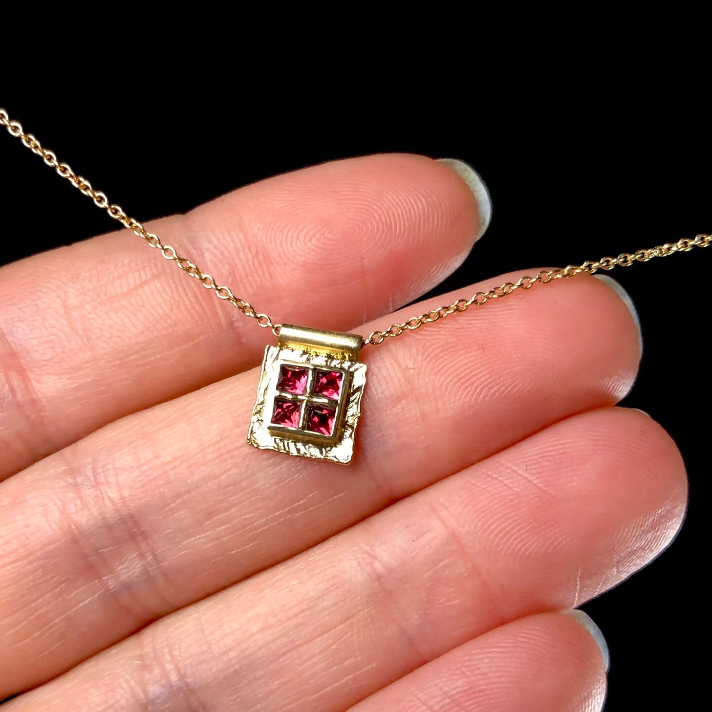 Four red spinel stones in square gold platform on chain shown in hand