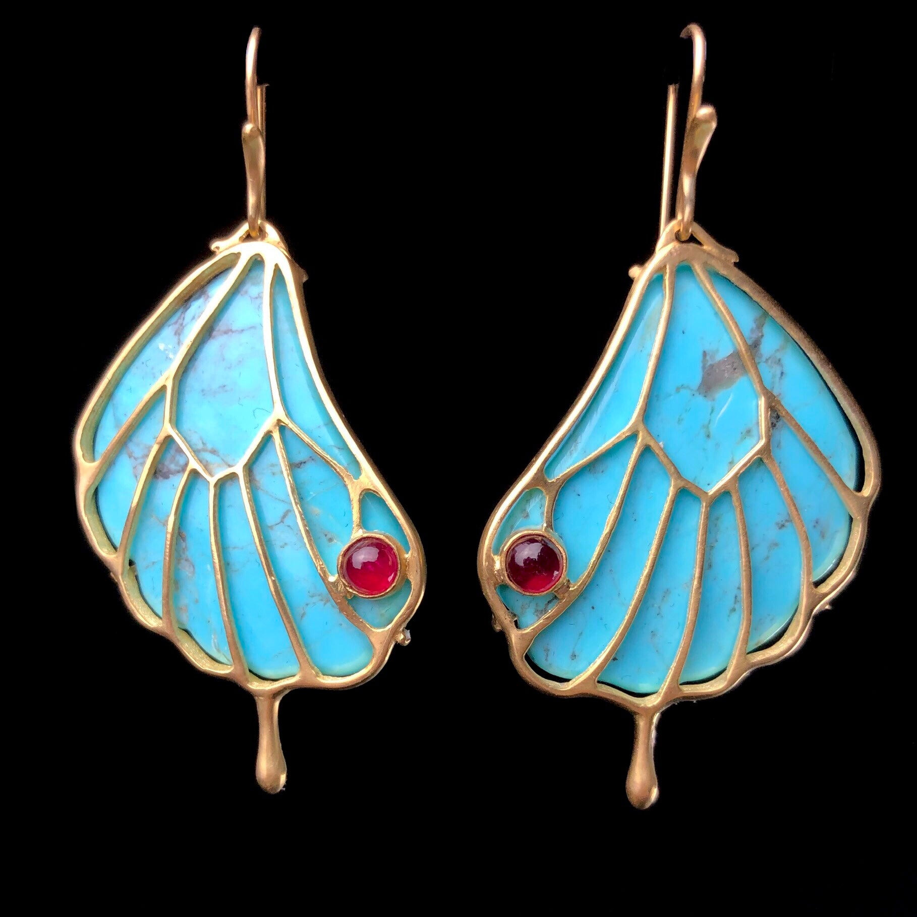 Turquoise stones in gold framework shaped like butterfly wings with round red ruby accent on earring hooks