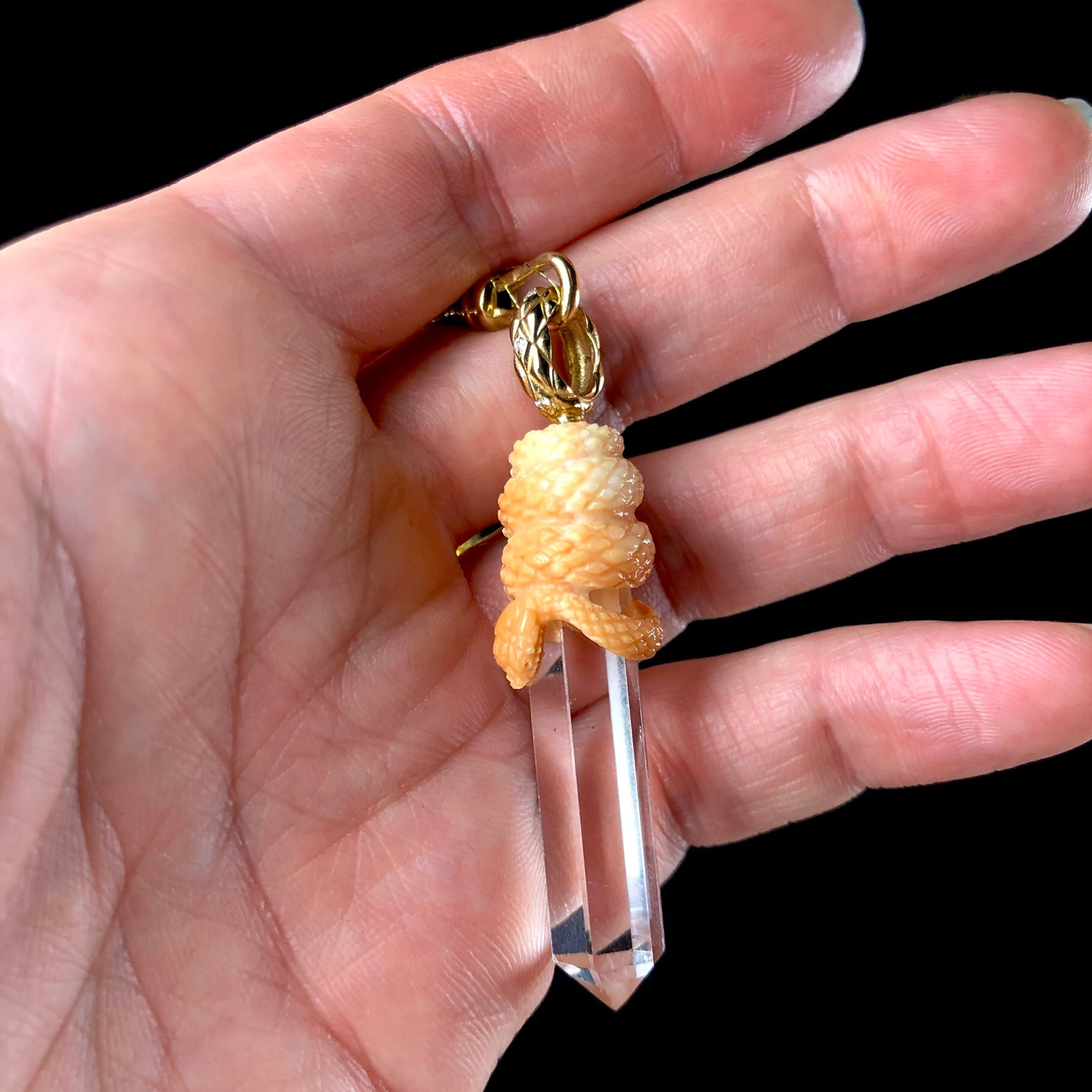 Clear crystal with light orange snake coiled about its top with gold bail shown in hand