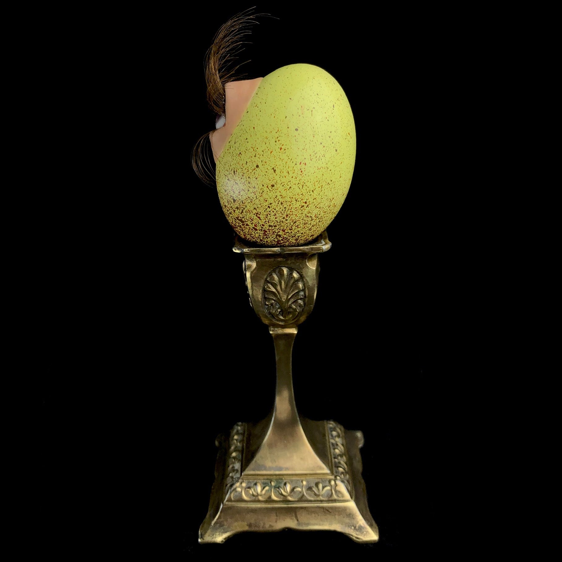Side view of yellow egg with long eyelashes sitting on brass stand