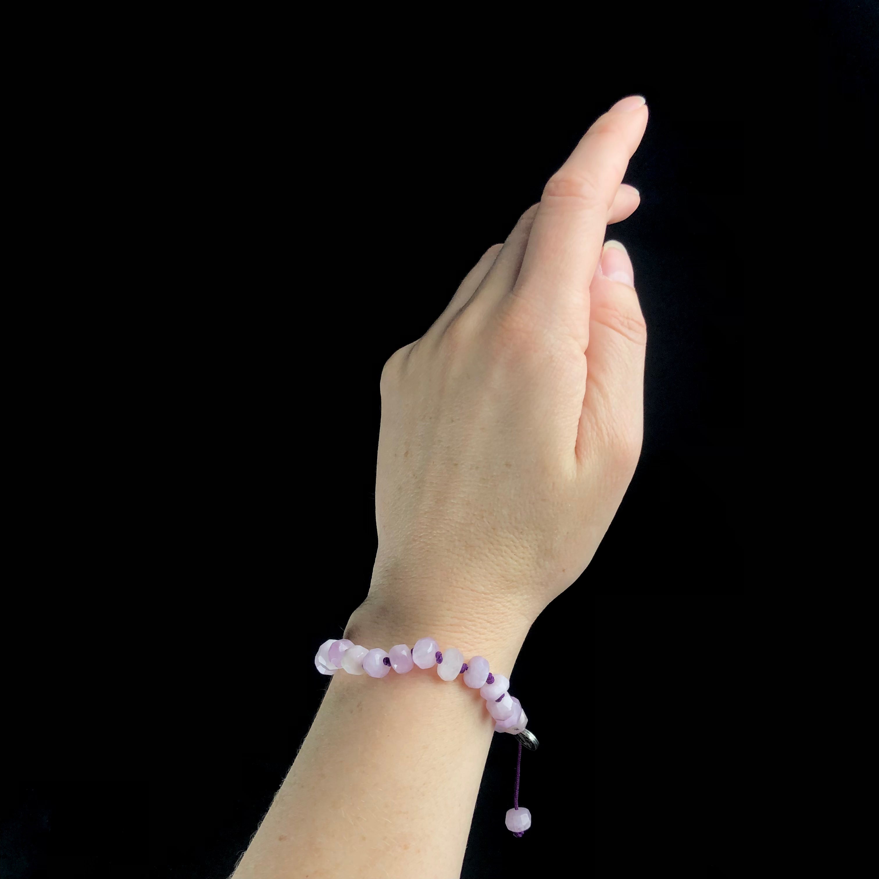 Opaque pink faceted stone beaded bracelet knotted with purple cord shown worn on wrist