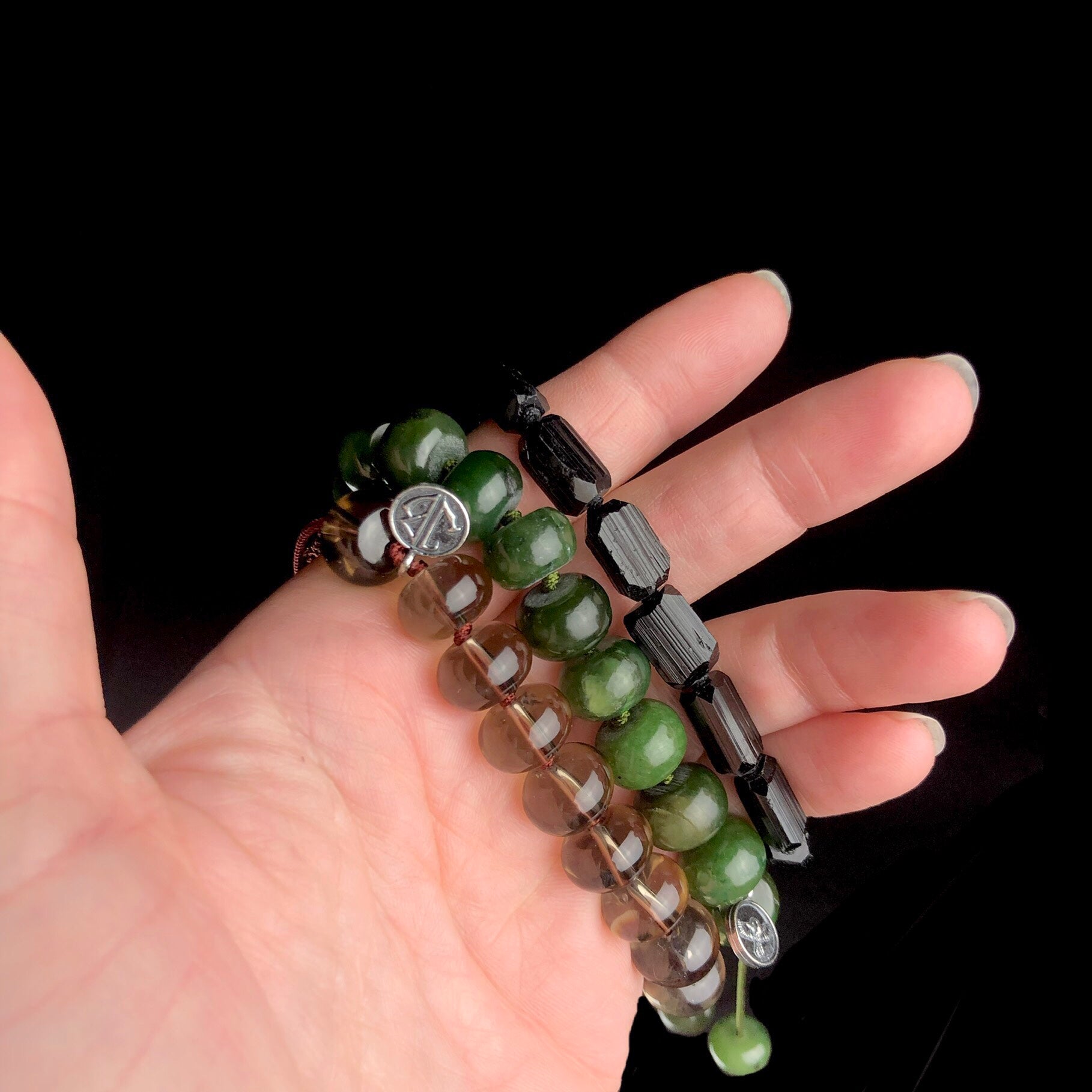 Transparent grey, opaque green and dark black stone beaded bracelets shown side by side on hand.