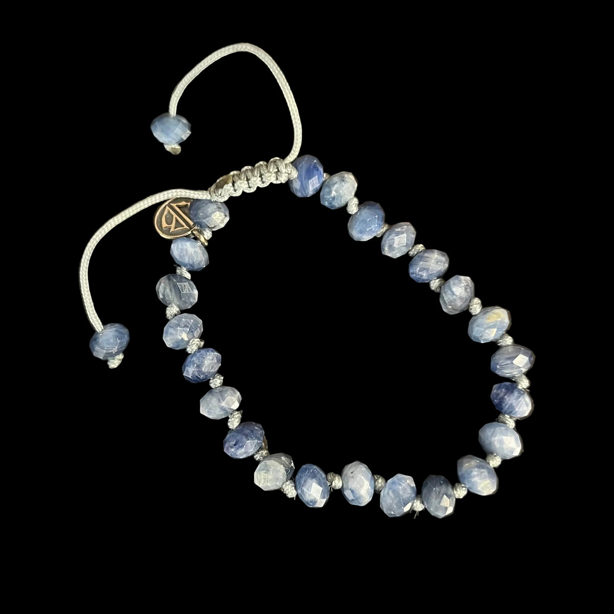 A beaded stretch bracelet with faceted blue sapphire-like beads and a white adjustable cord, displayed on a black background. 