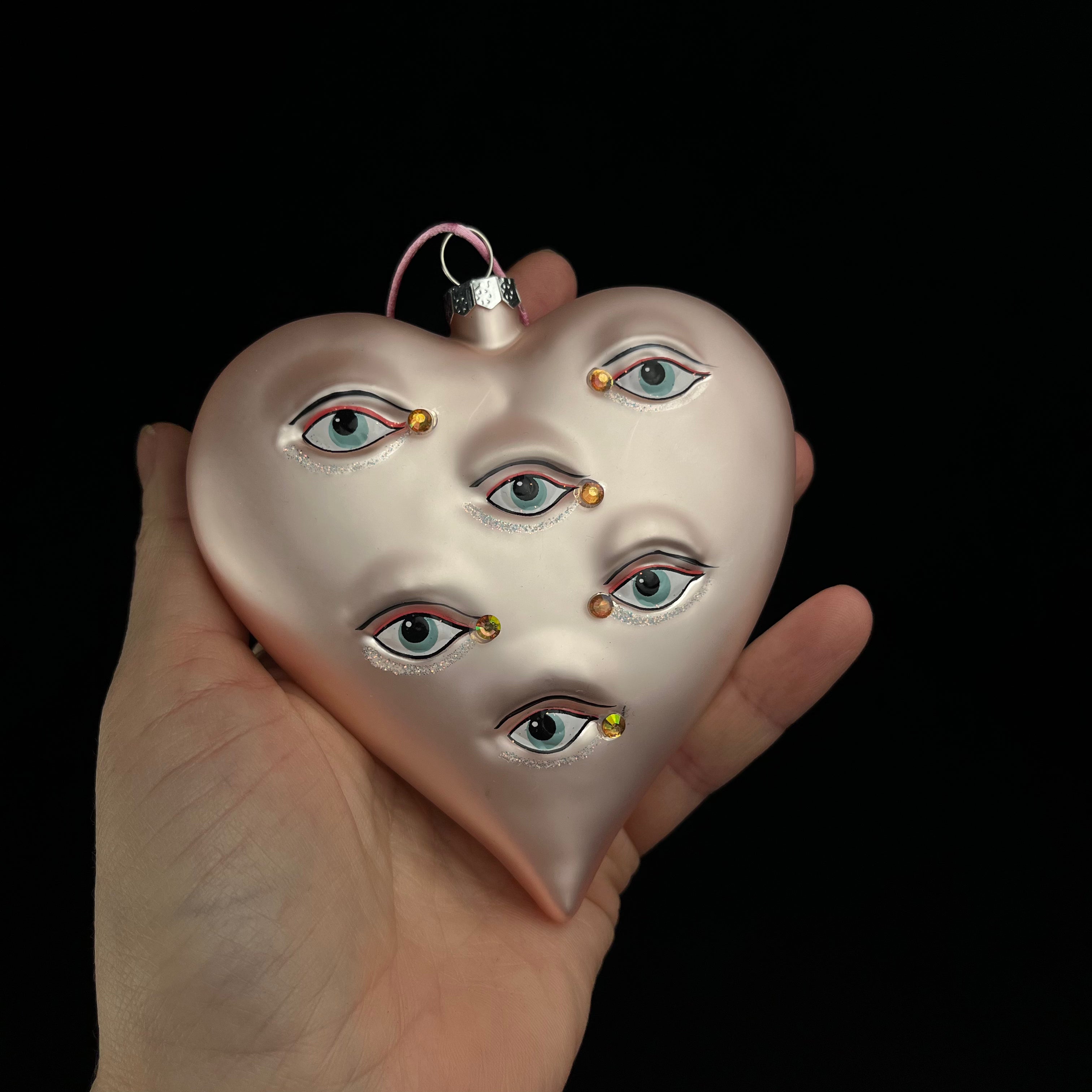 Heart-shaped ornament with painted eyes held in a hand against a black background