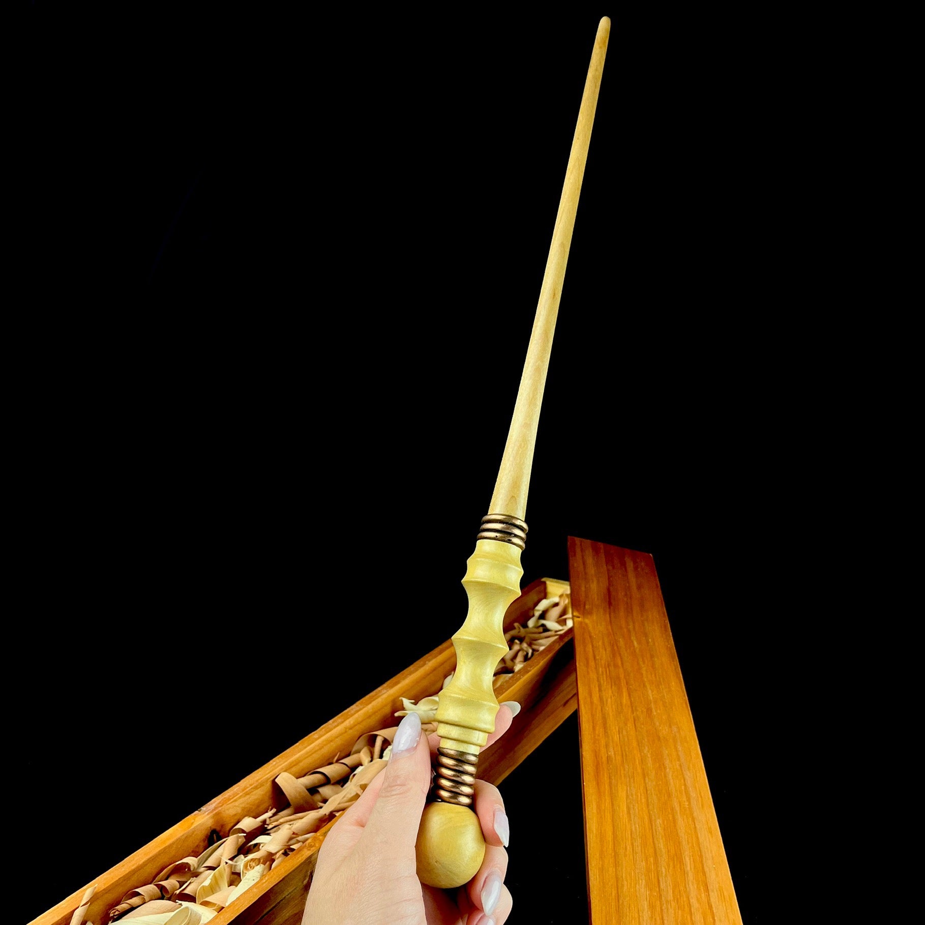 Light wood wand shown held in hand with box beneath