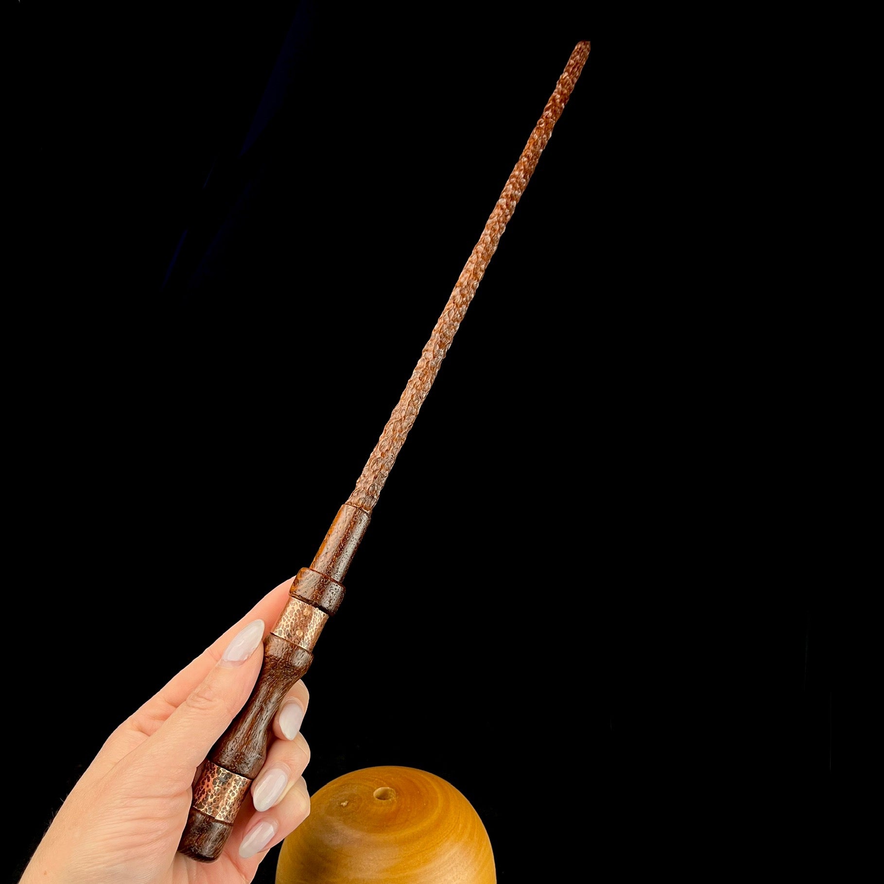 Heavily textured dark wood wand shown held in hand