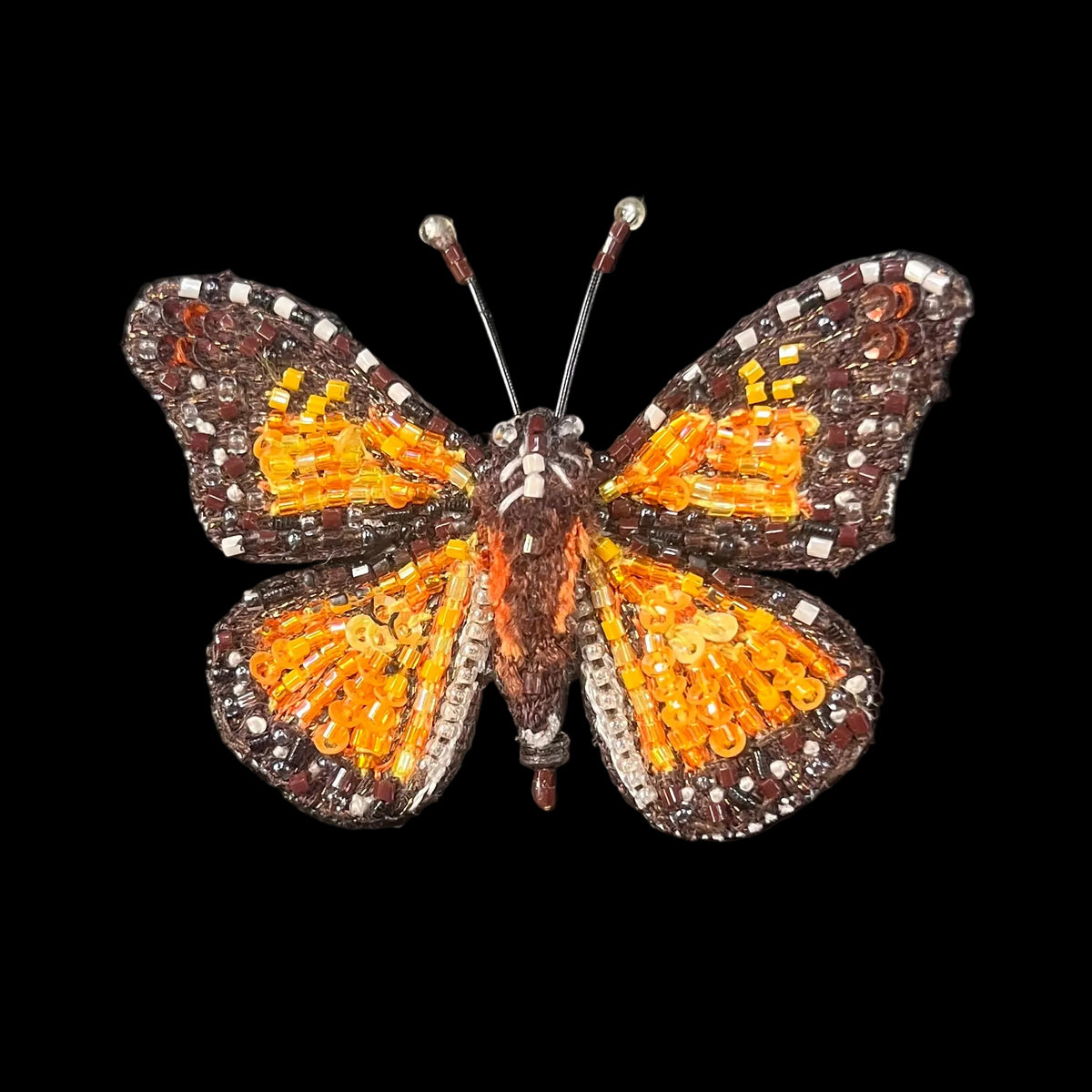 Orange, brown and white beads sewn to a felted butterfly shape in lifelike realism 
