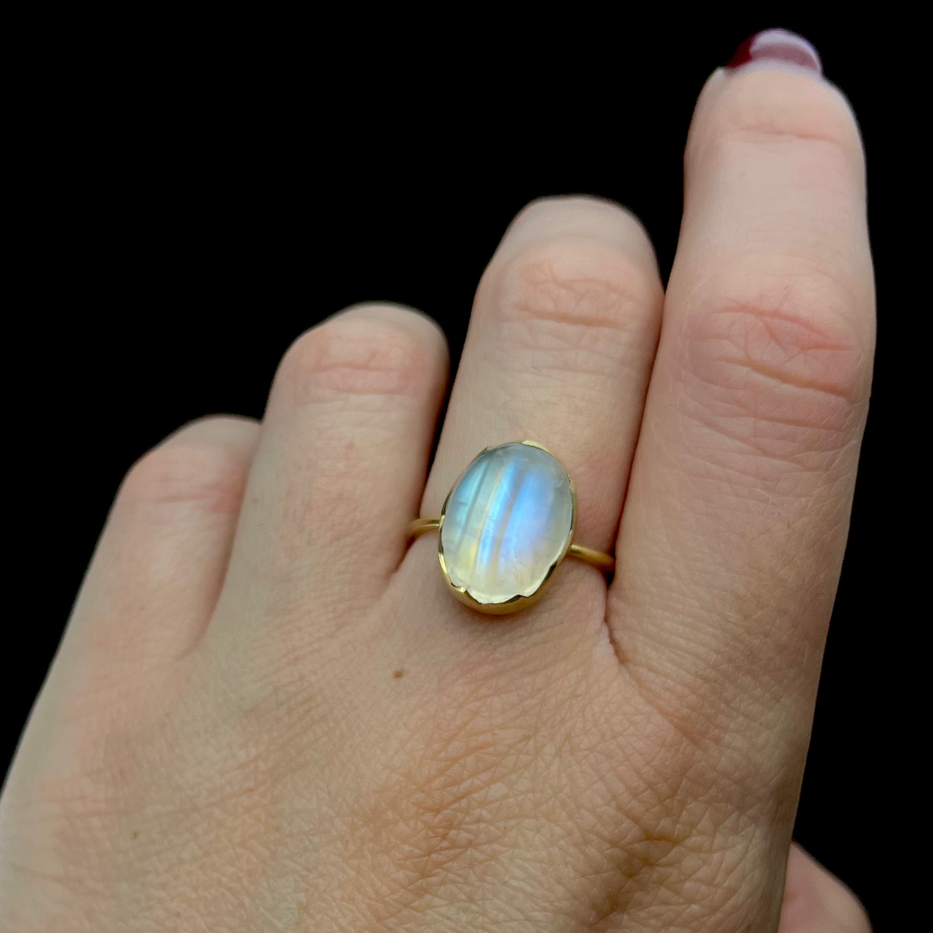 Gold ring with a large gemstone on a hand against a black background