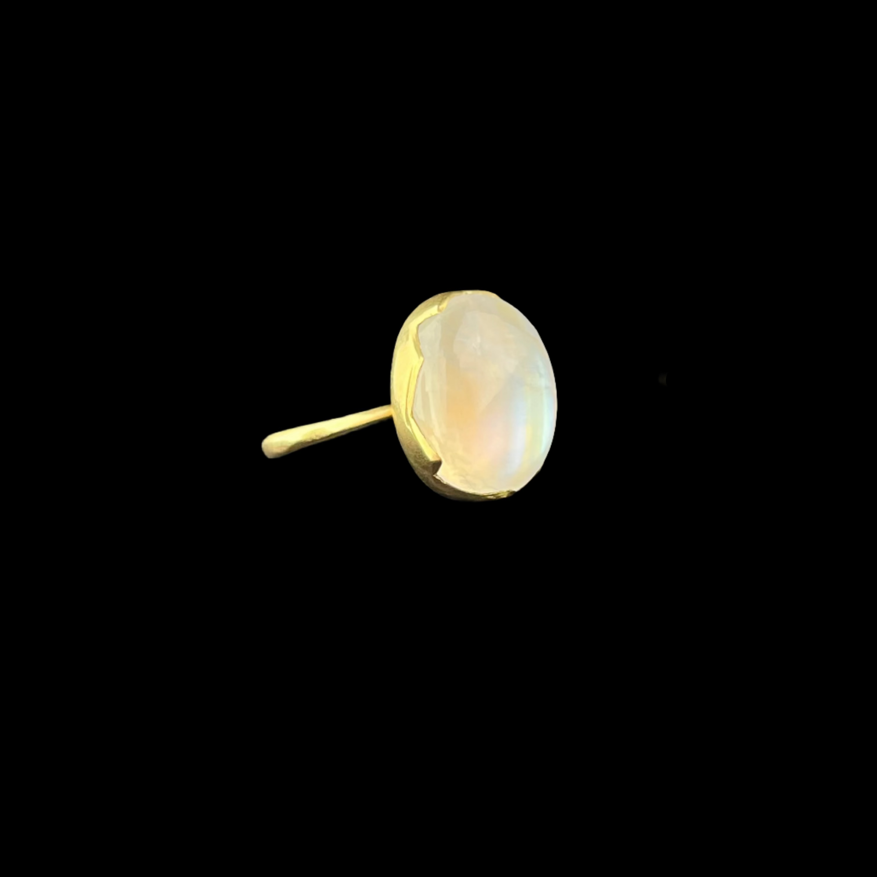 Gold ring with a large white stone on a black stand against a dark background