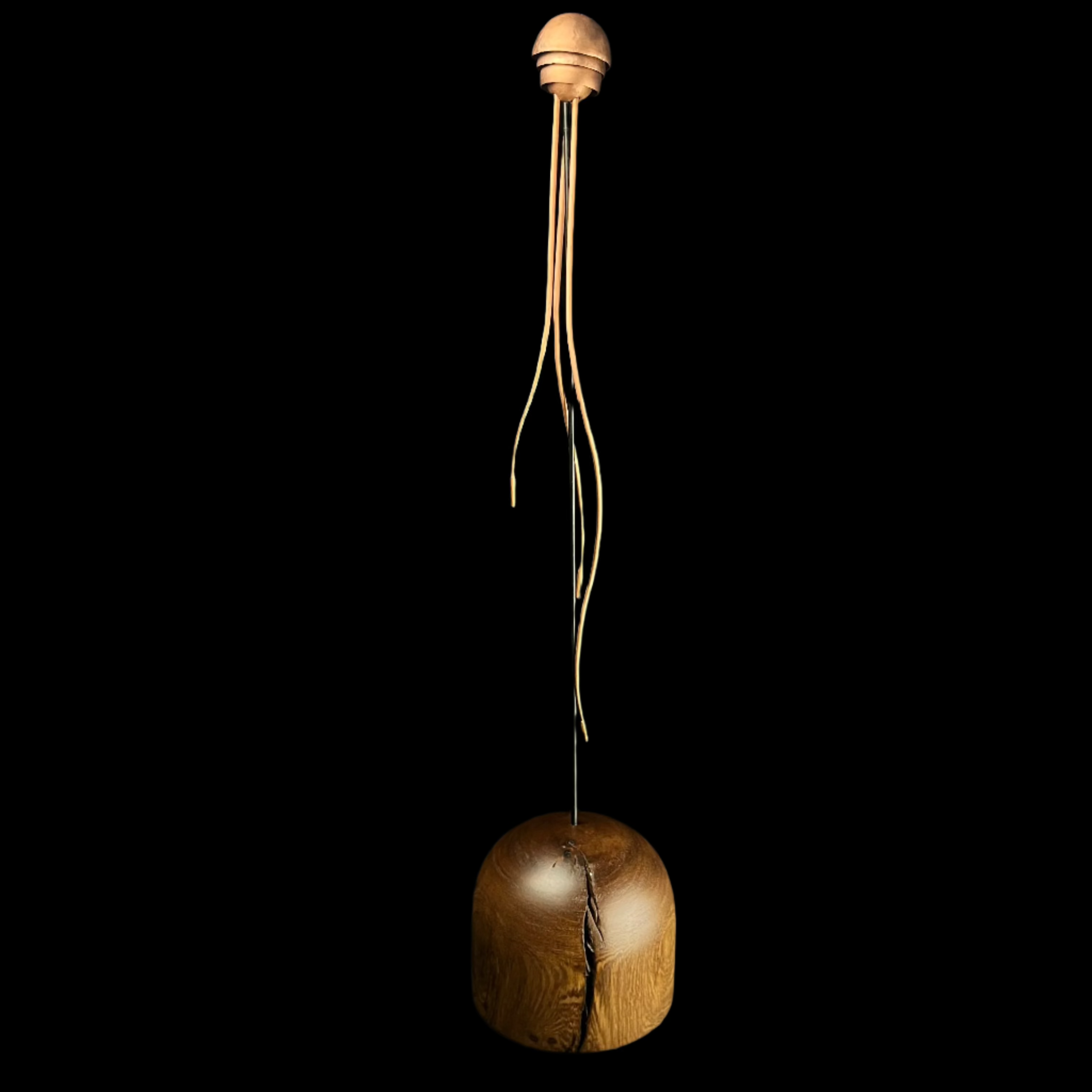 Wooden sculpture with a cracked base and hanging elements on a dark background