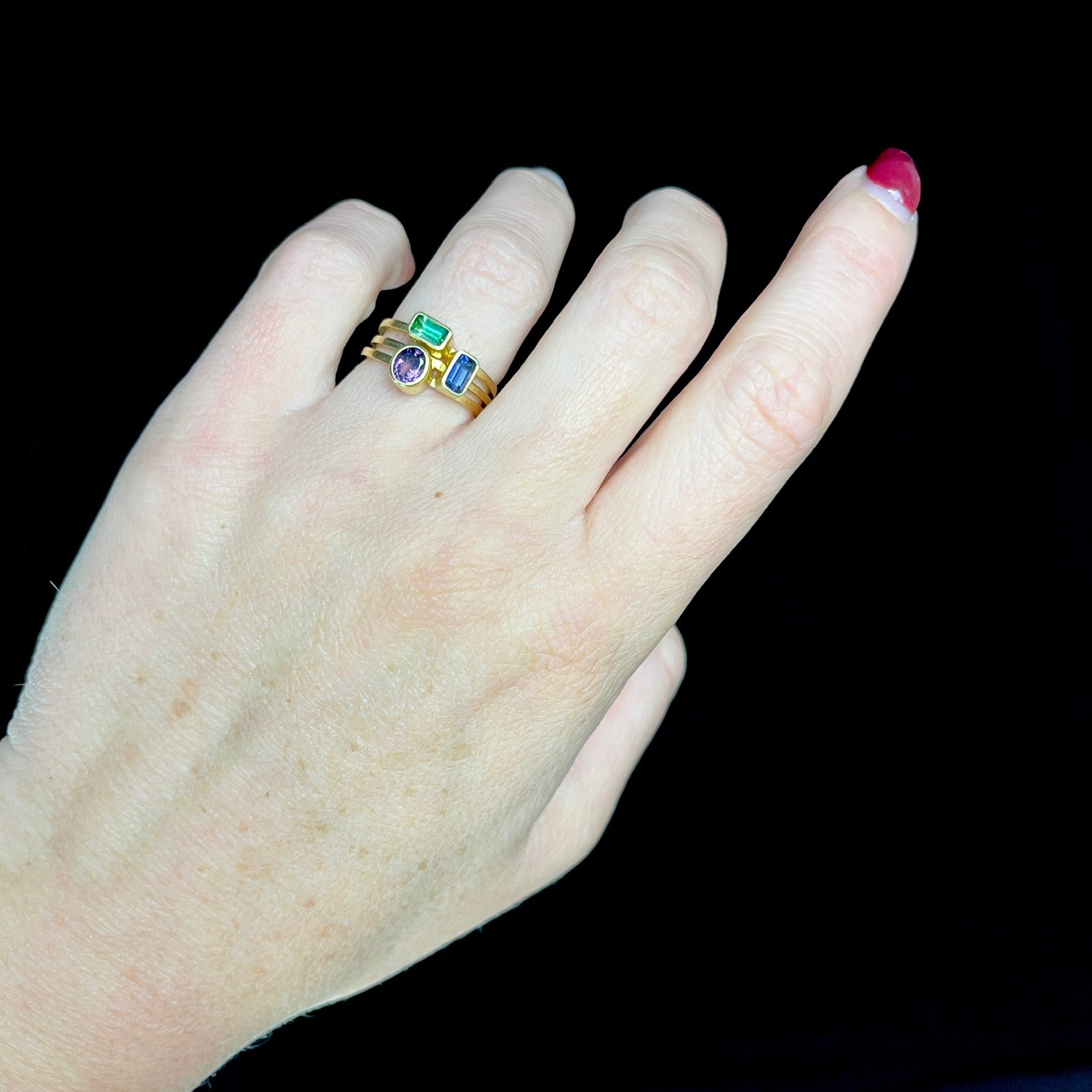 Hand wearing a gold ring with gemstones on a black background