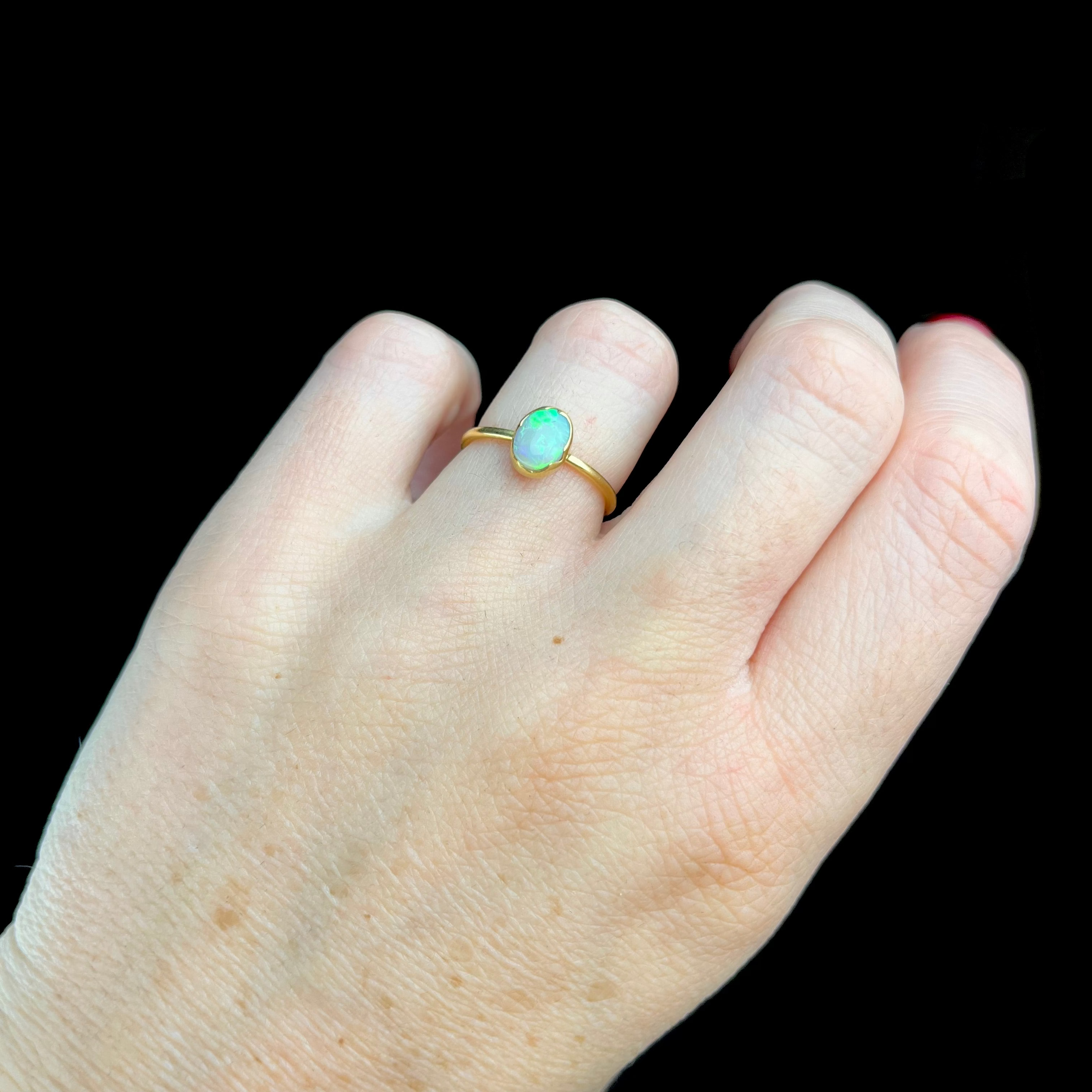 Hand wearing a gold ring with an opal stone against a black background