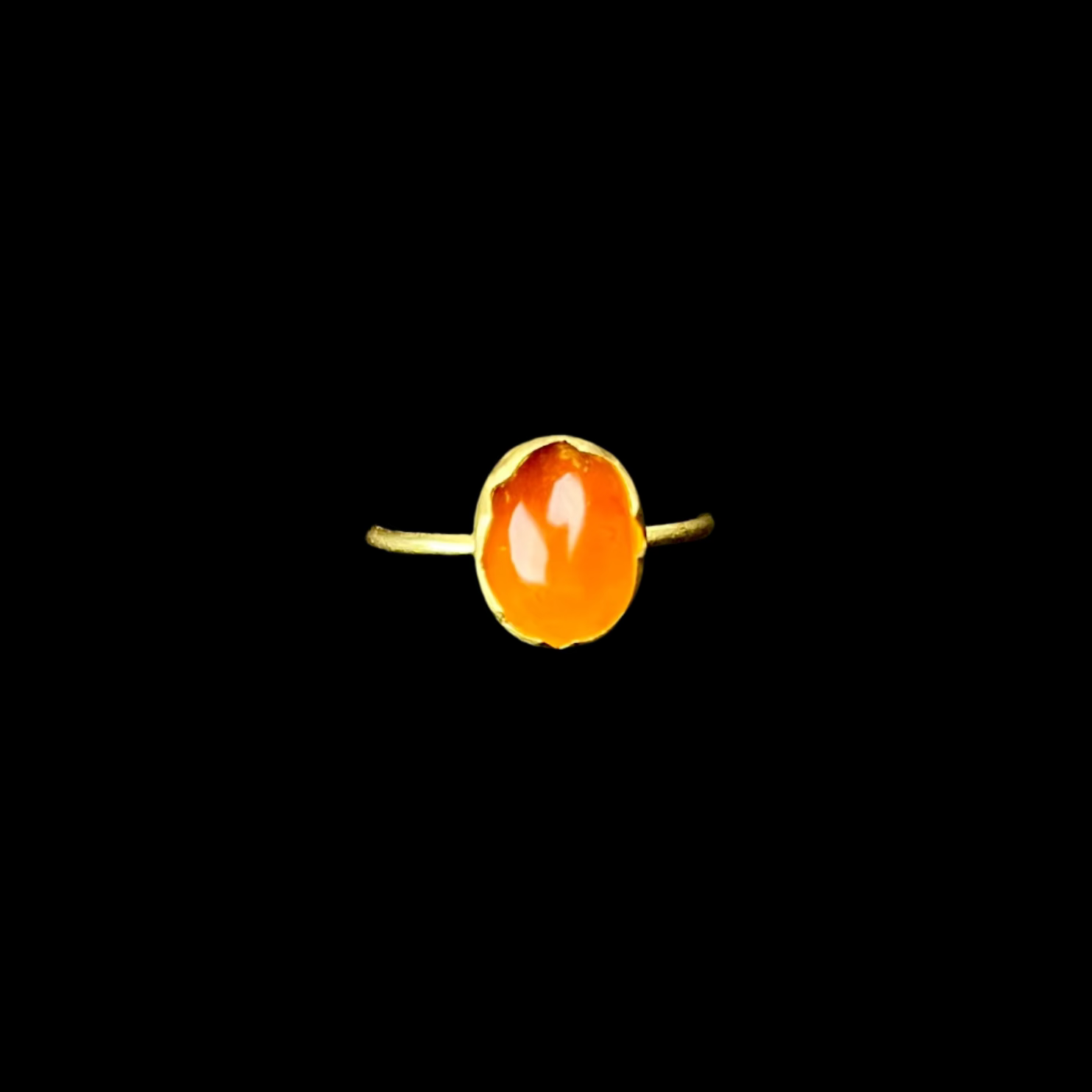 Gold ring with a large orange gemstone on a black background