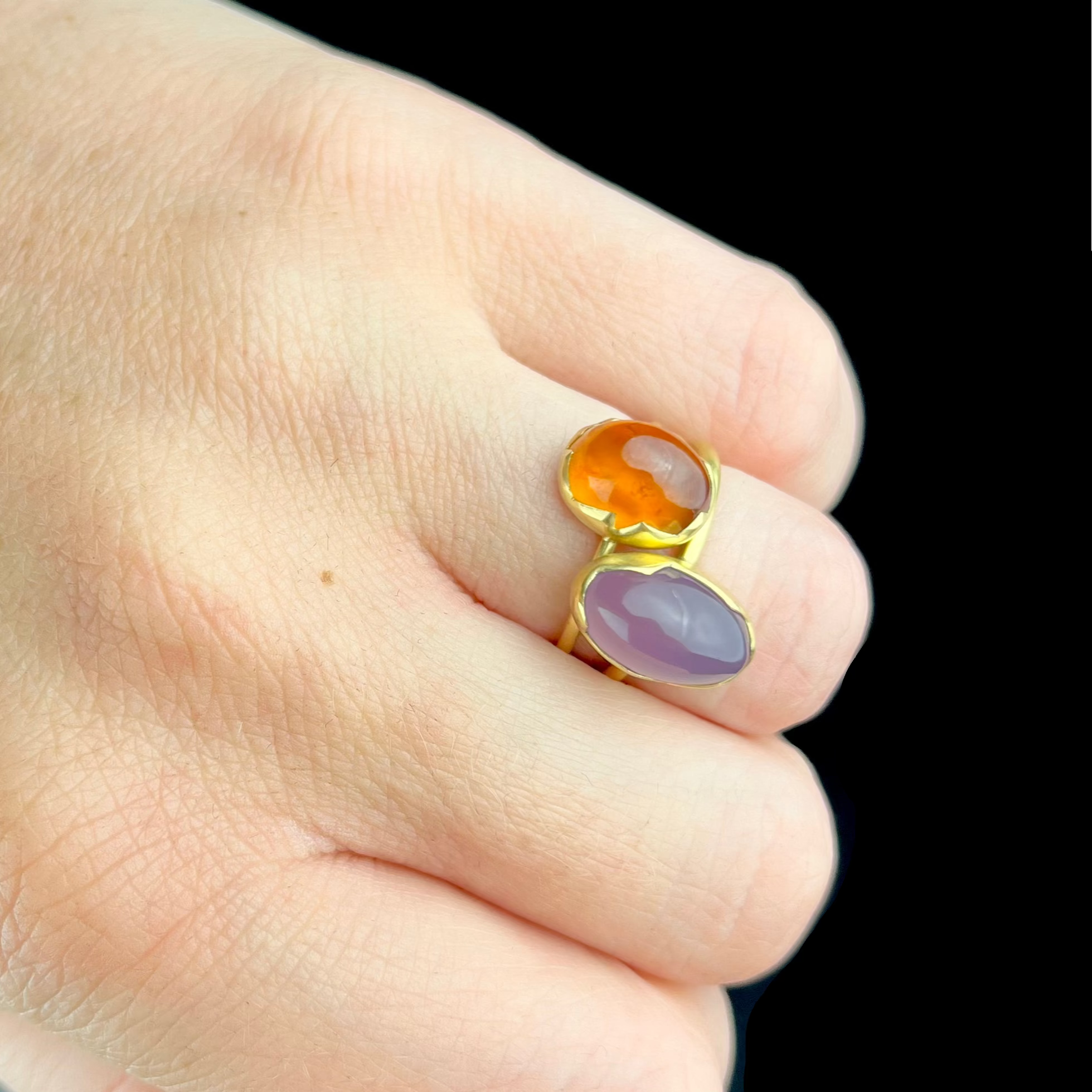 Gold ring with orange and purple stones on a finger against a dark background