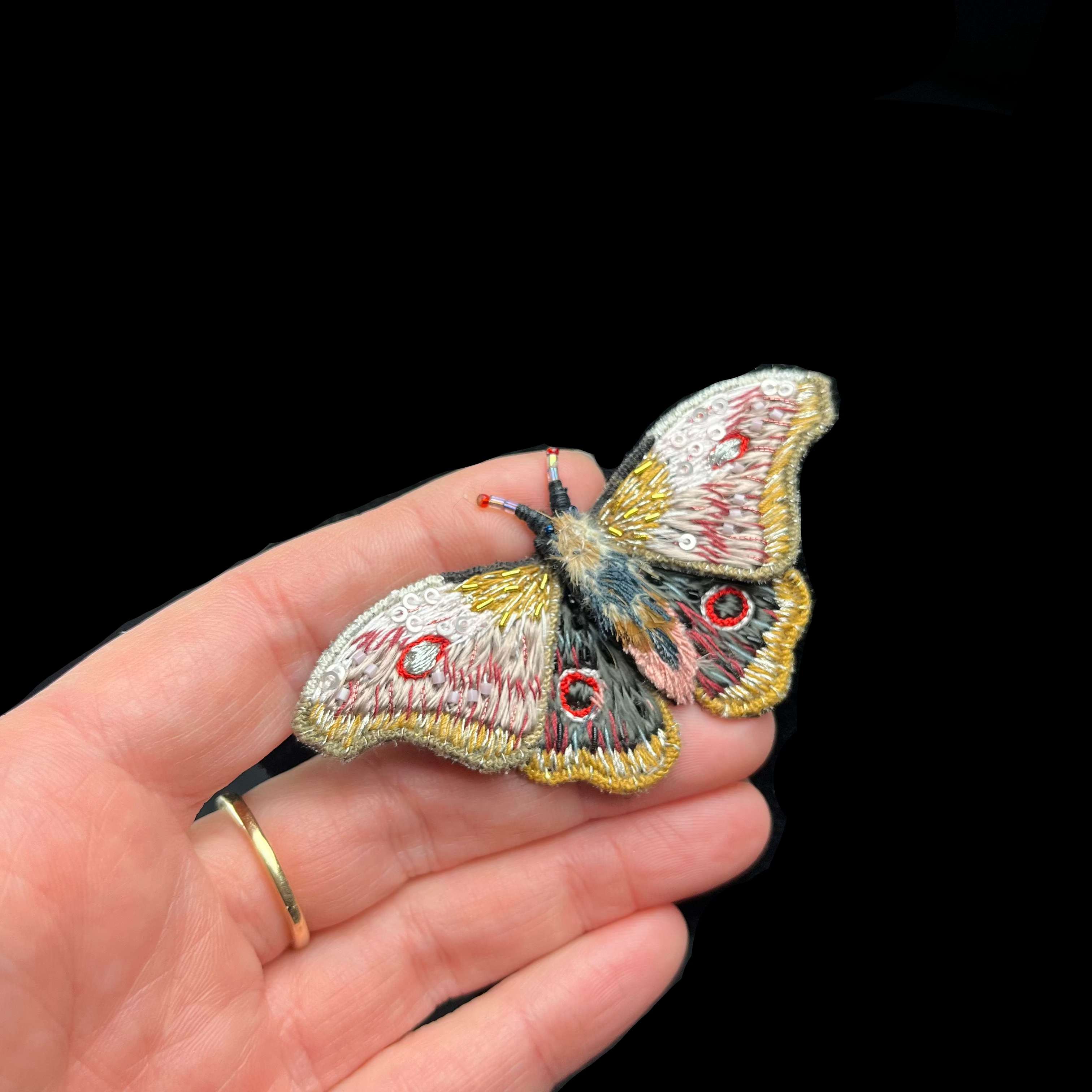 Embroidered butterfly patch held in a hand against a dark background