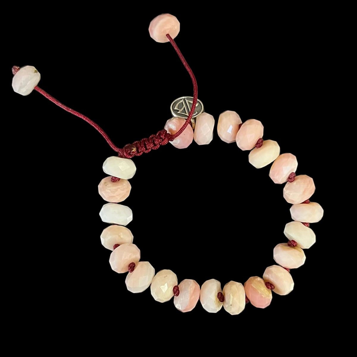 A beaded stretch bracelet made of light pink and white oval beads with a red cord and toggle, displayed on a dark, scratched surface.