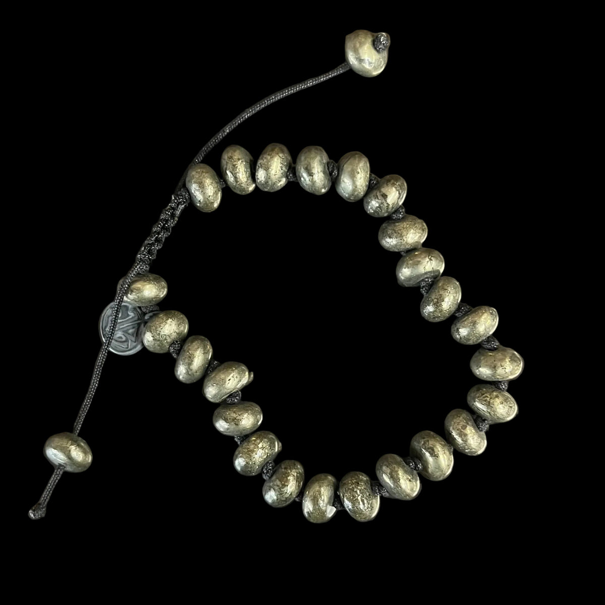 A beaded stretch bracelet made of metallic olive-green beads on a black cord, displayed on a dark, scratched metal surface.
