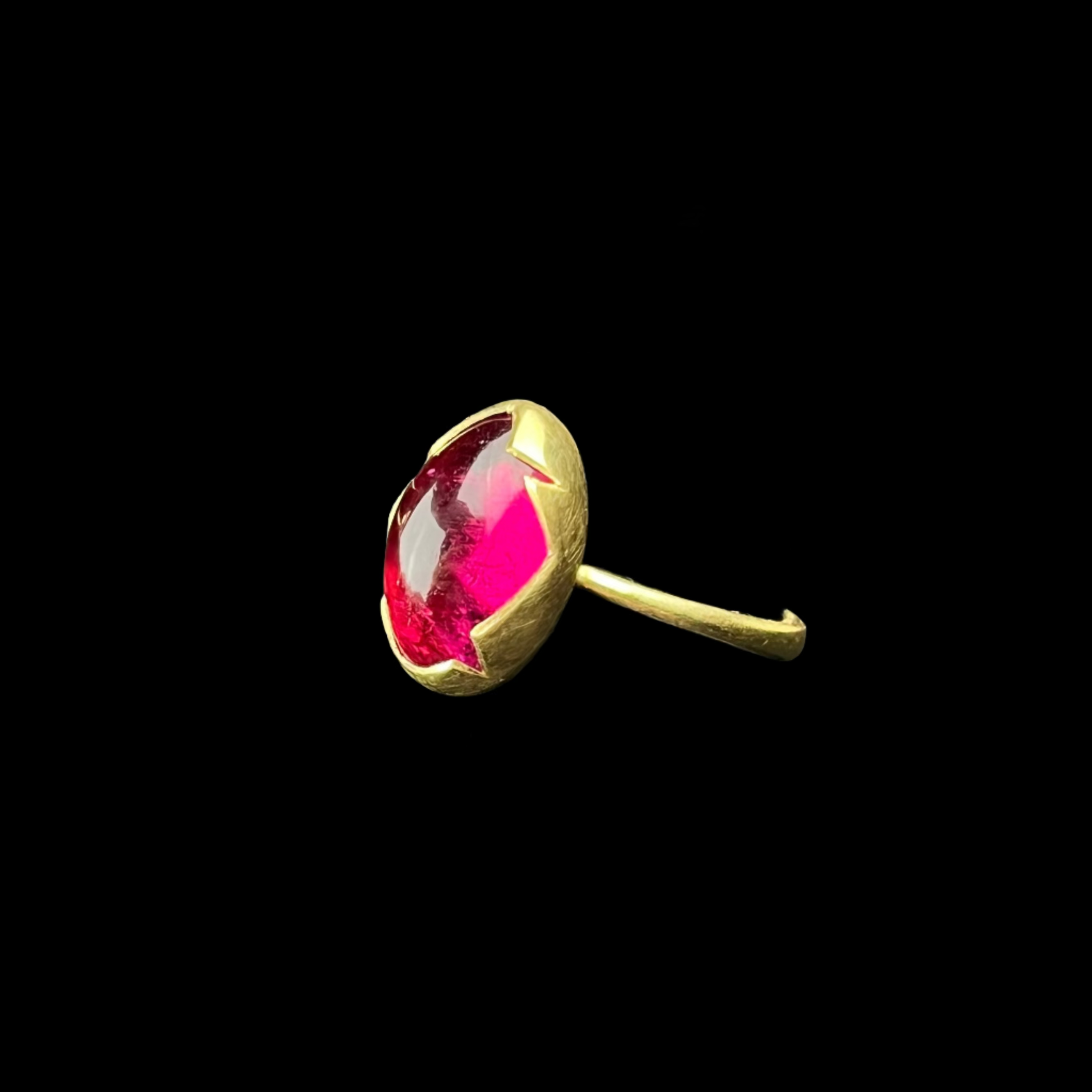Gold ring with a pink gemstone on a black stand against a dark background