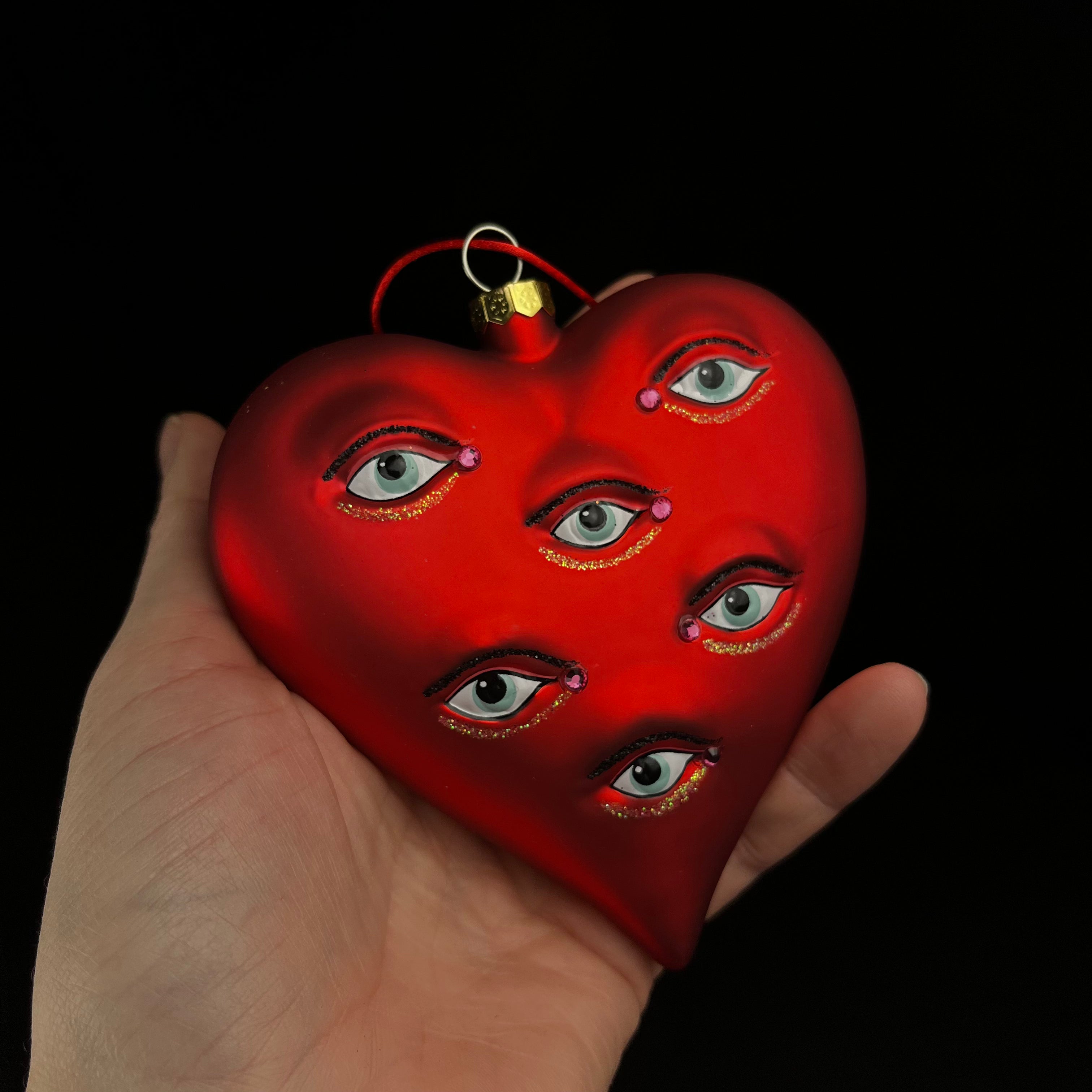 Red heart-shaped ornament with eyes on a black background