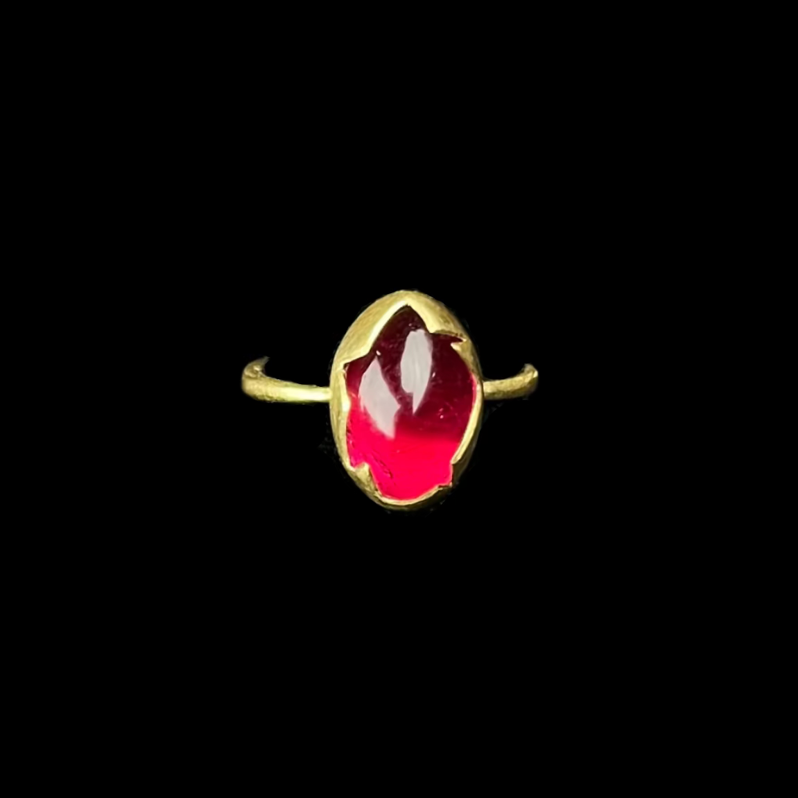 Gold ring with a red gemstone on a black stand against a dark background