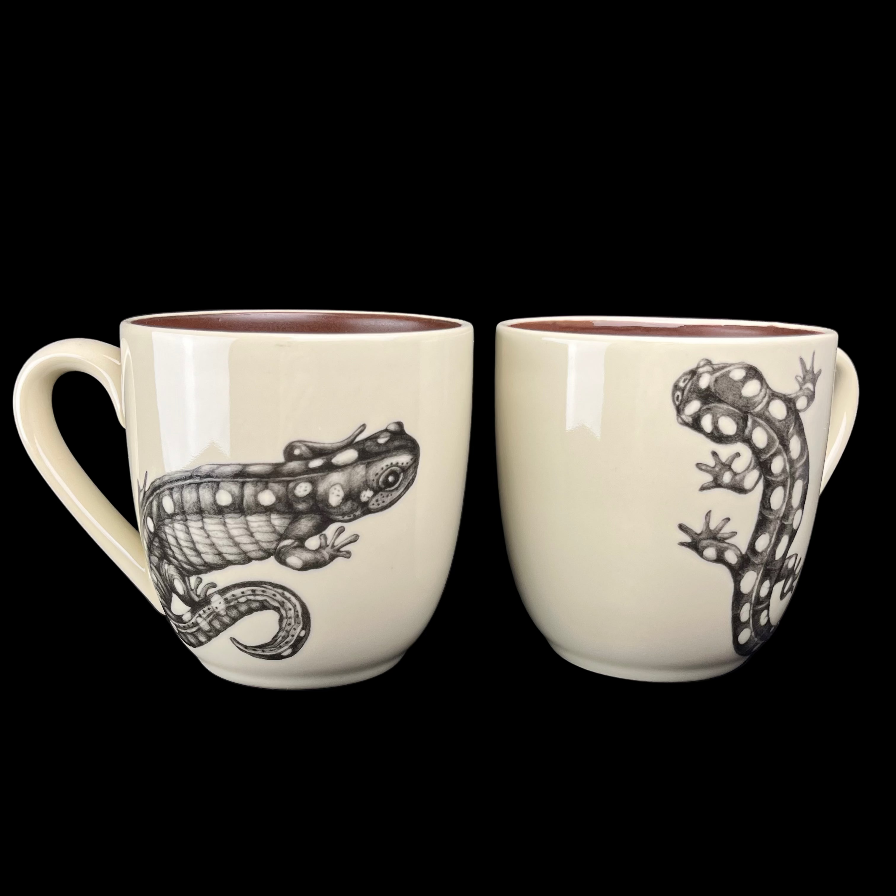 Two ceramic mugs with lizard designs on a dark background