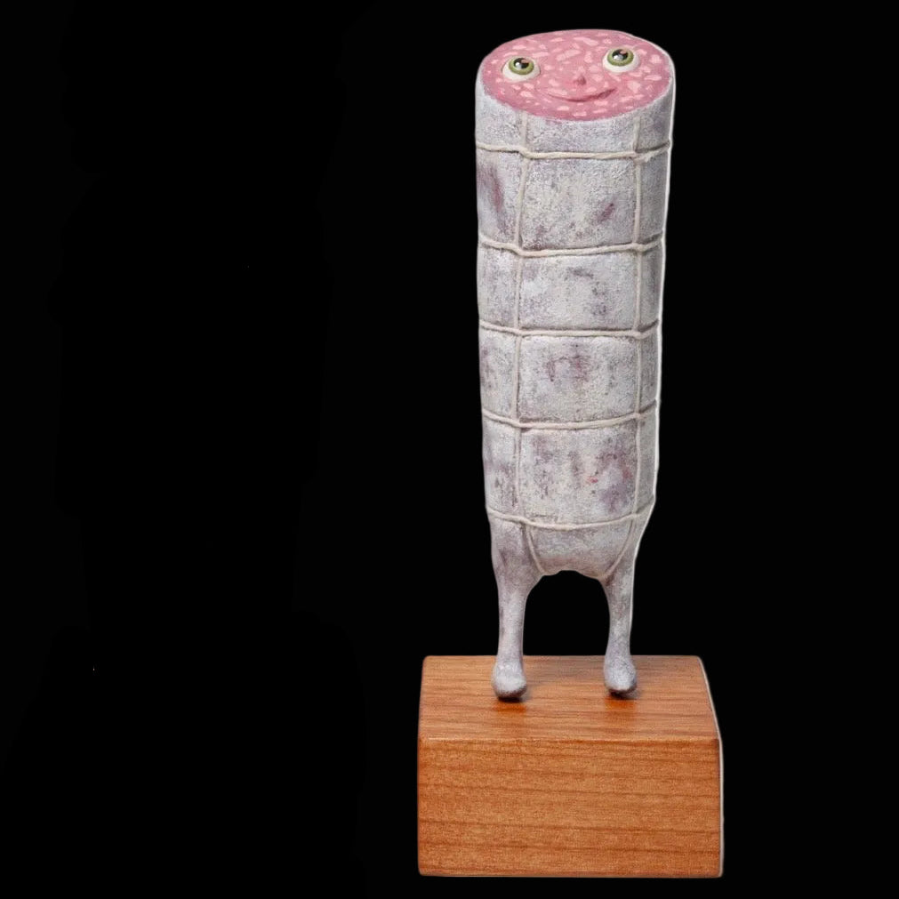 Smiling salami sculpture with eyes and feet on wooden block