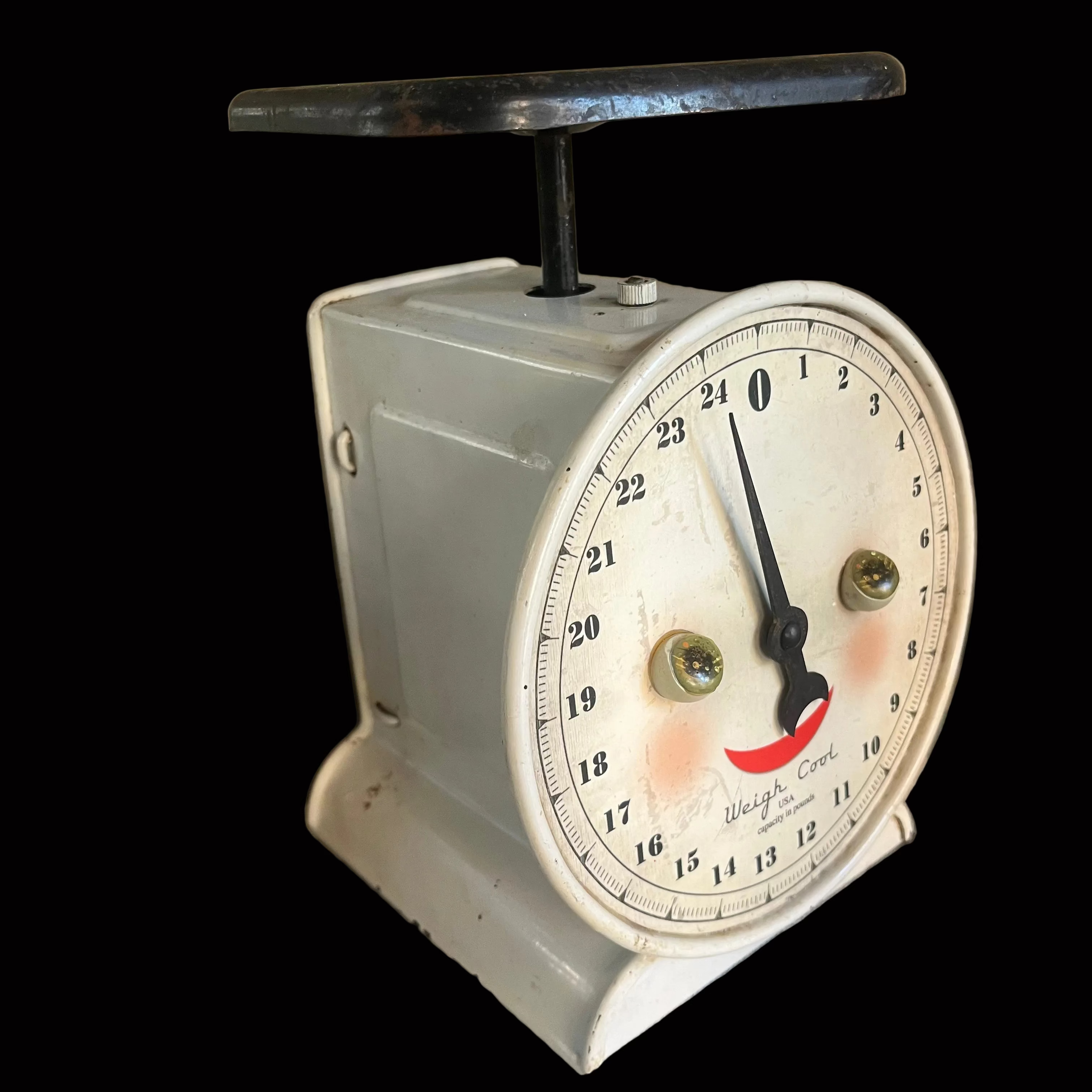 A vintage analog kitchen scale with a white face, black pointer, and a light gray painted metal body, sitting on a blue-and-white checkered tablecloth.