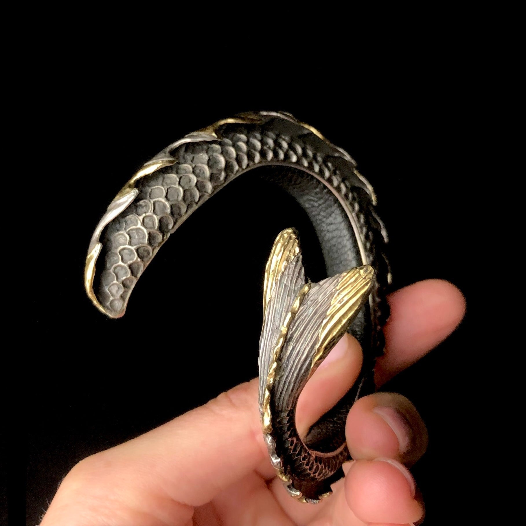 Hand holding a metallic fish-shaped keychain against a black background
