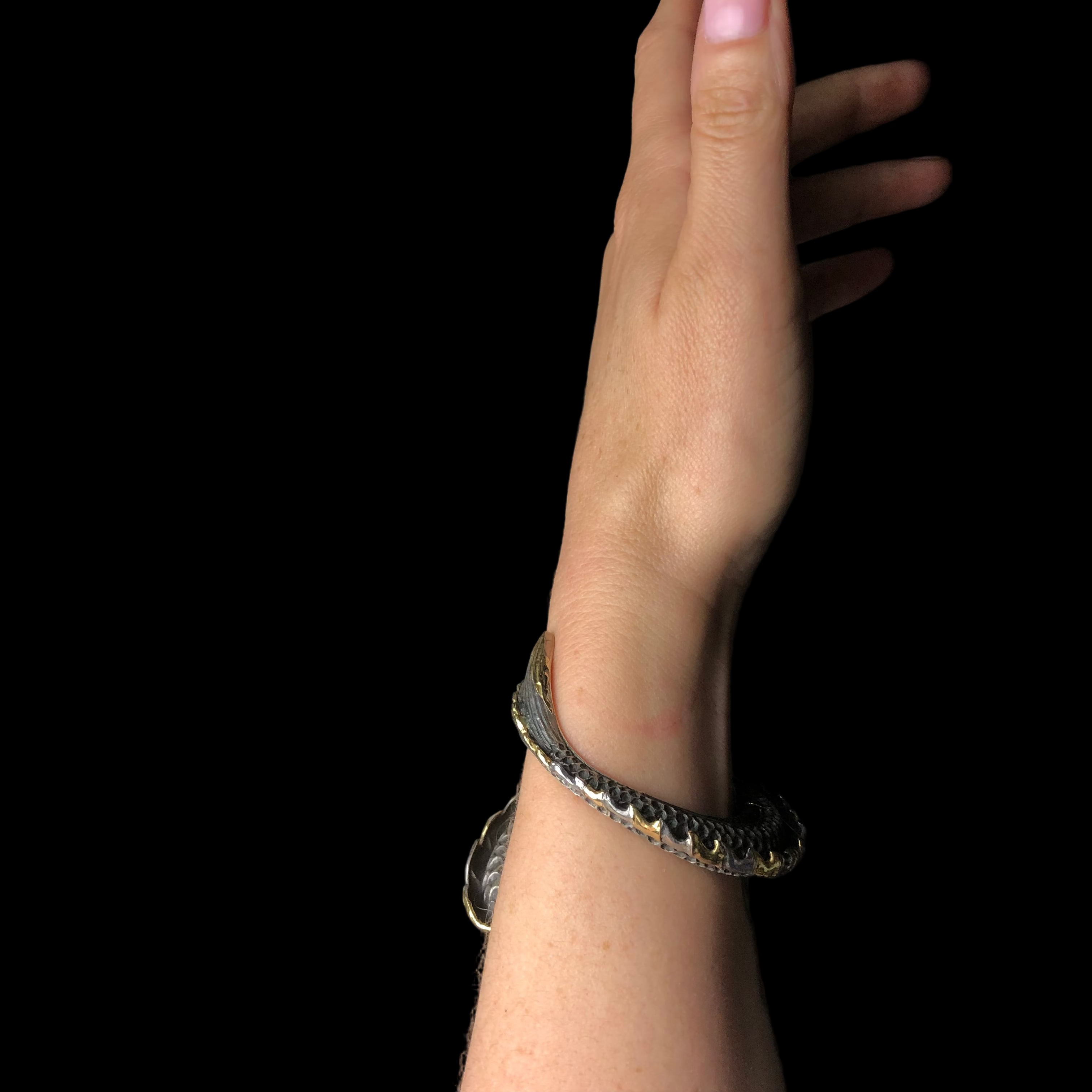 Wrist shown wearing a silver bracelet wrapping around from front to back on black background