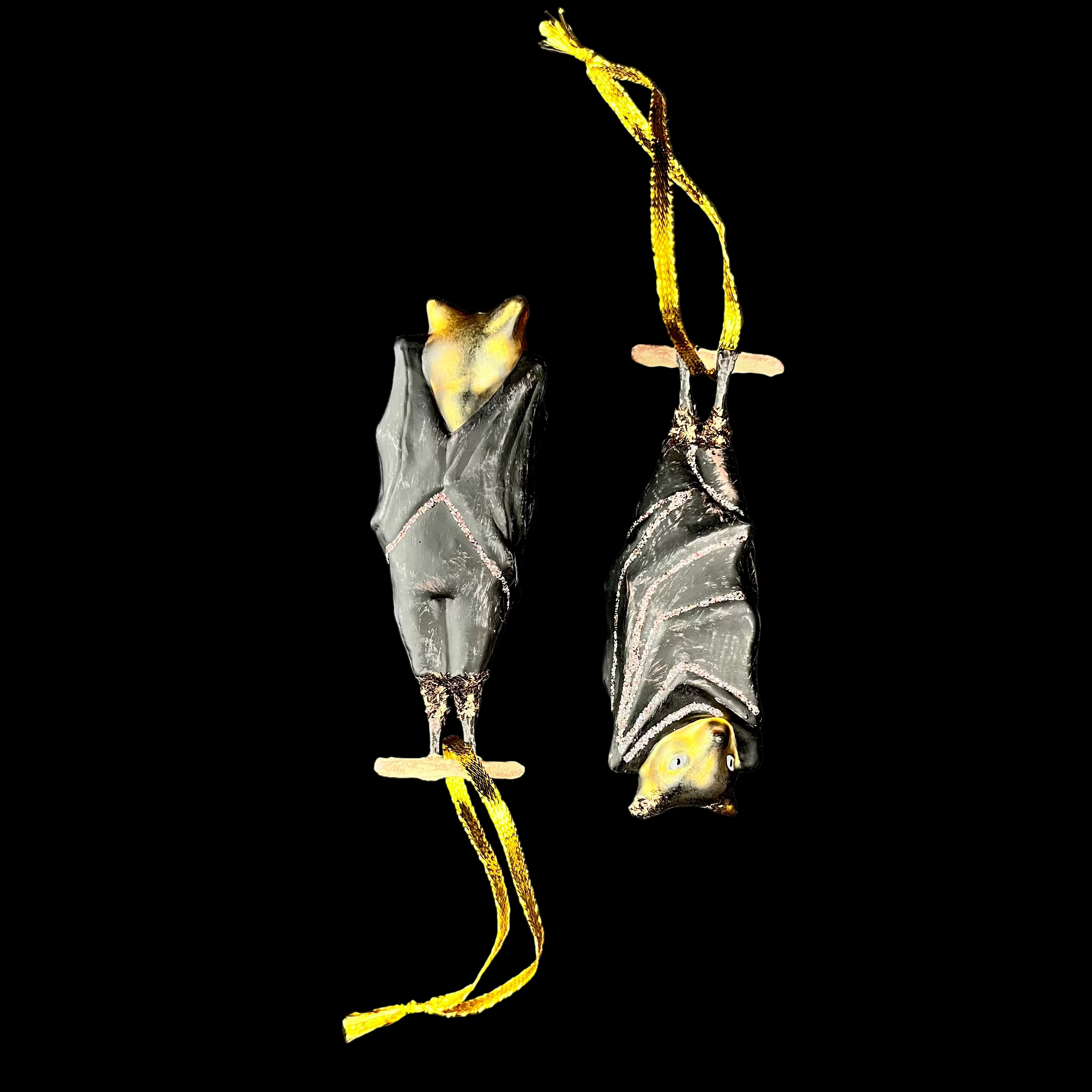 Two bat-shaped ornaments with yellow strings on a dark background