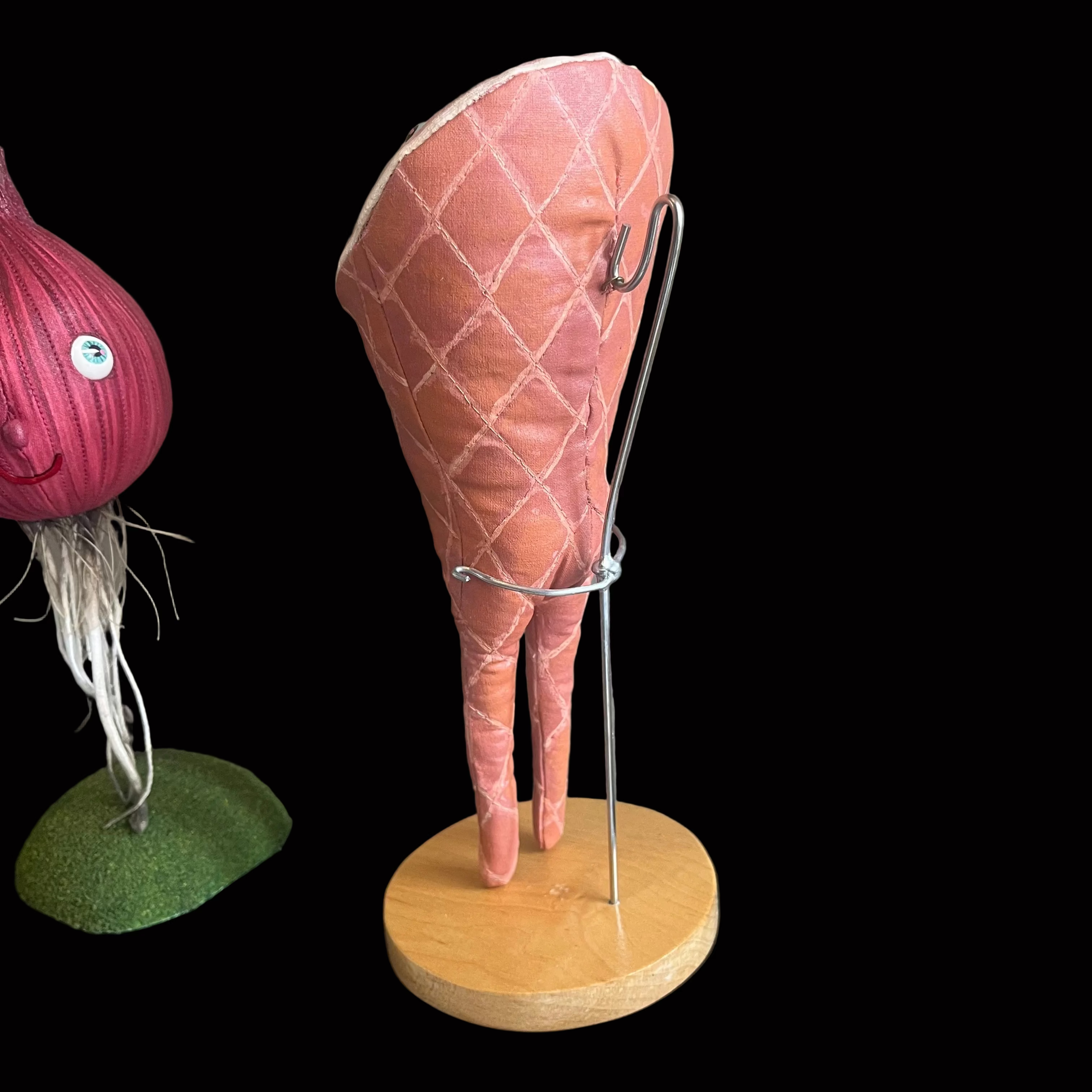Back view of a stuffed smoked ham-shaped decorative figure standing on wooden base with metal hook and brace shown against black background.