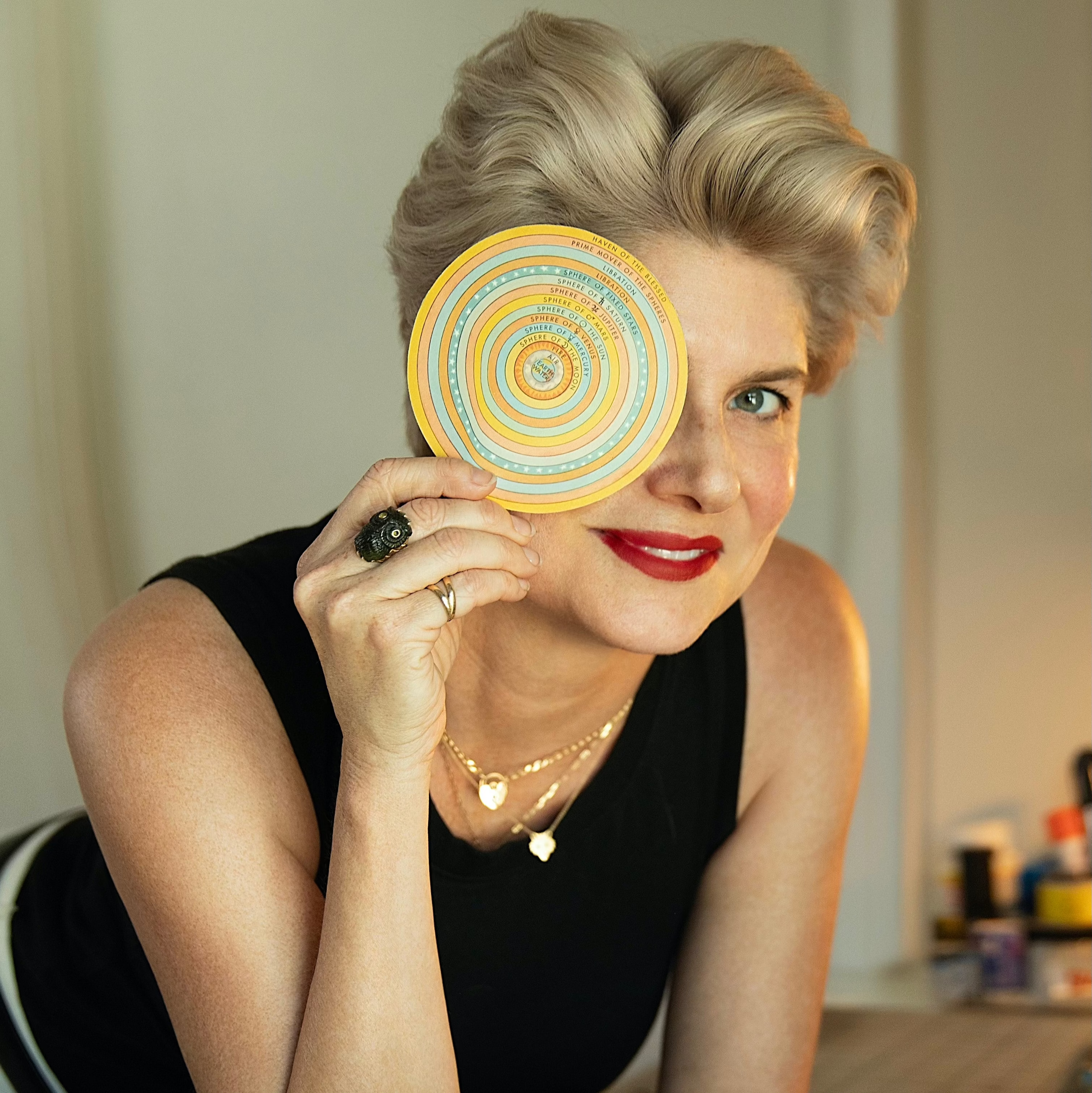 Woman holding a circular object with concentric circles, sitting at a table with various items.