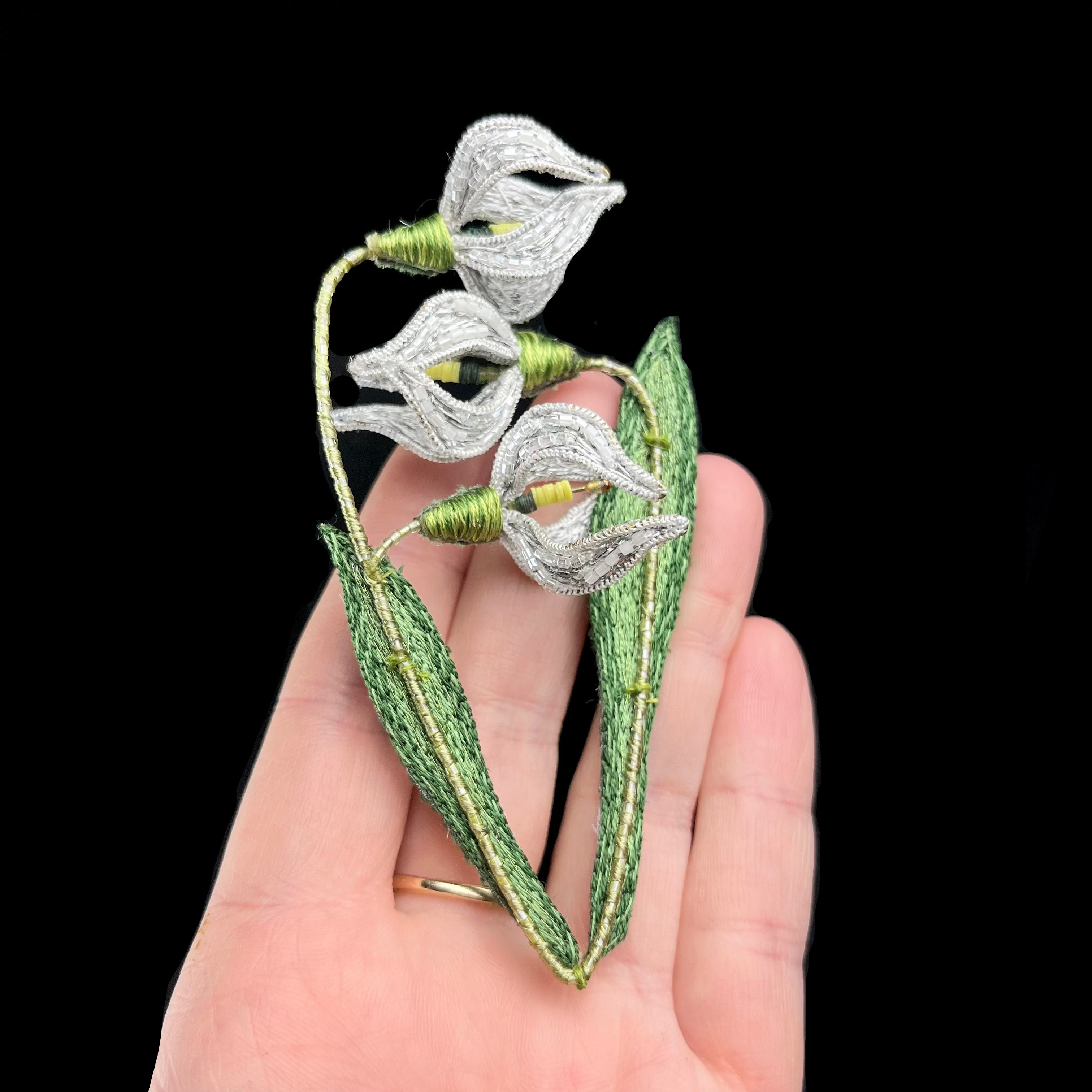 Silver flower brooch held against a hand with a black background