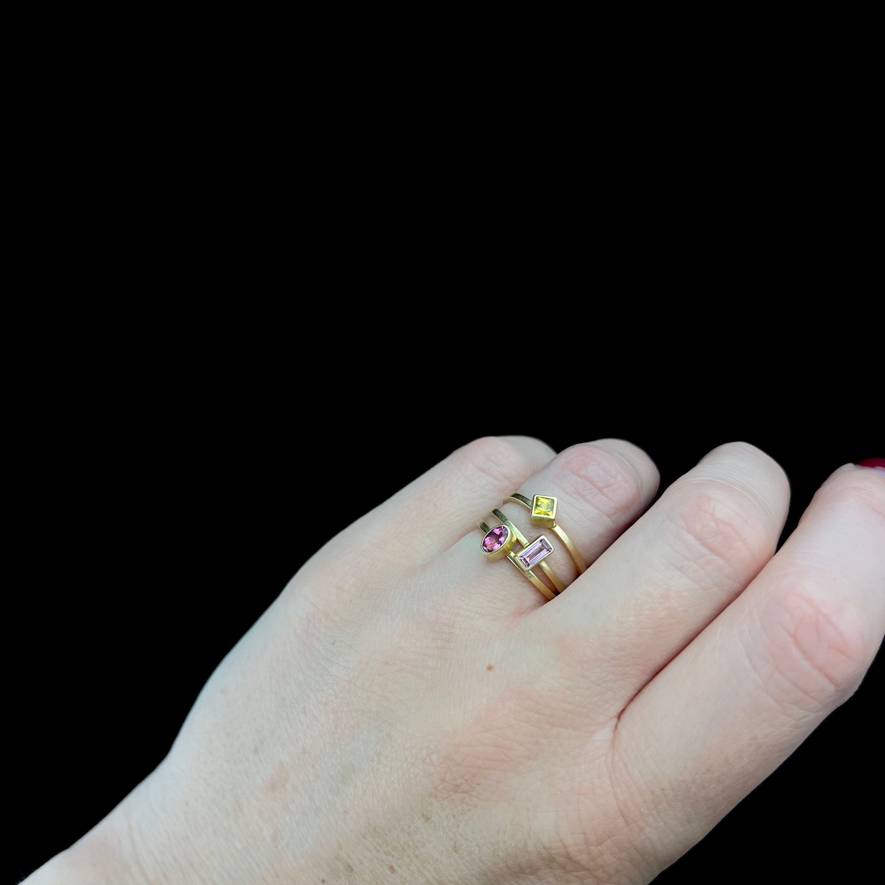 Hand wearing two gold rings with gemstones on a black background
