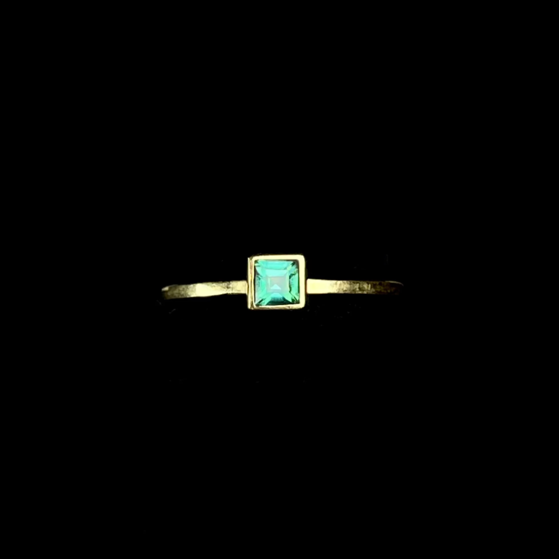 Gold ring with a green gemstone on a black stand